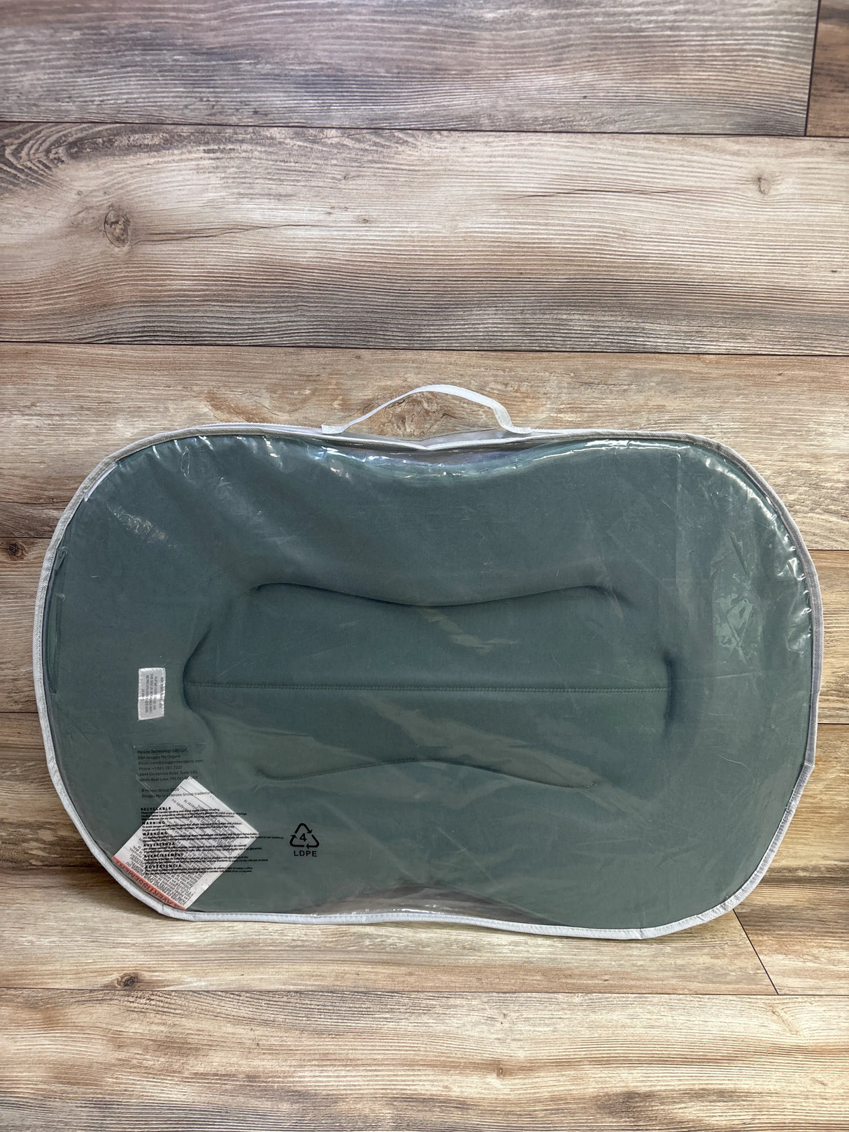 Top-down view of Snuggle Me Curve Lite baby lounger with moss cover in clear bag showing handle and contoured interior