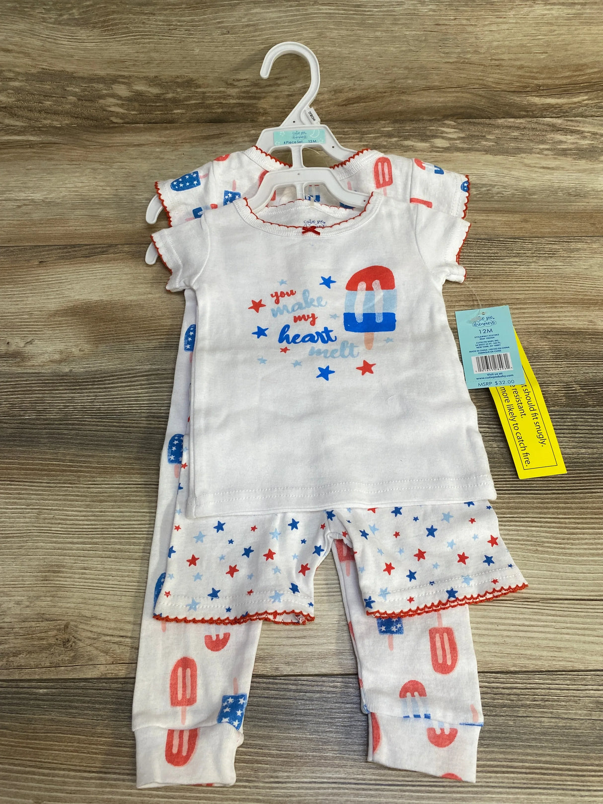 Front view of white 4-piece baby pajama set (12M) showcasing a short-sleeve top printed 'you make my heart melt' and star-and-popsicle pants on a wood surface