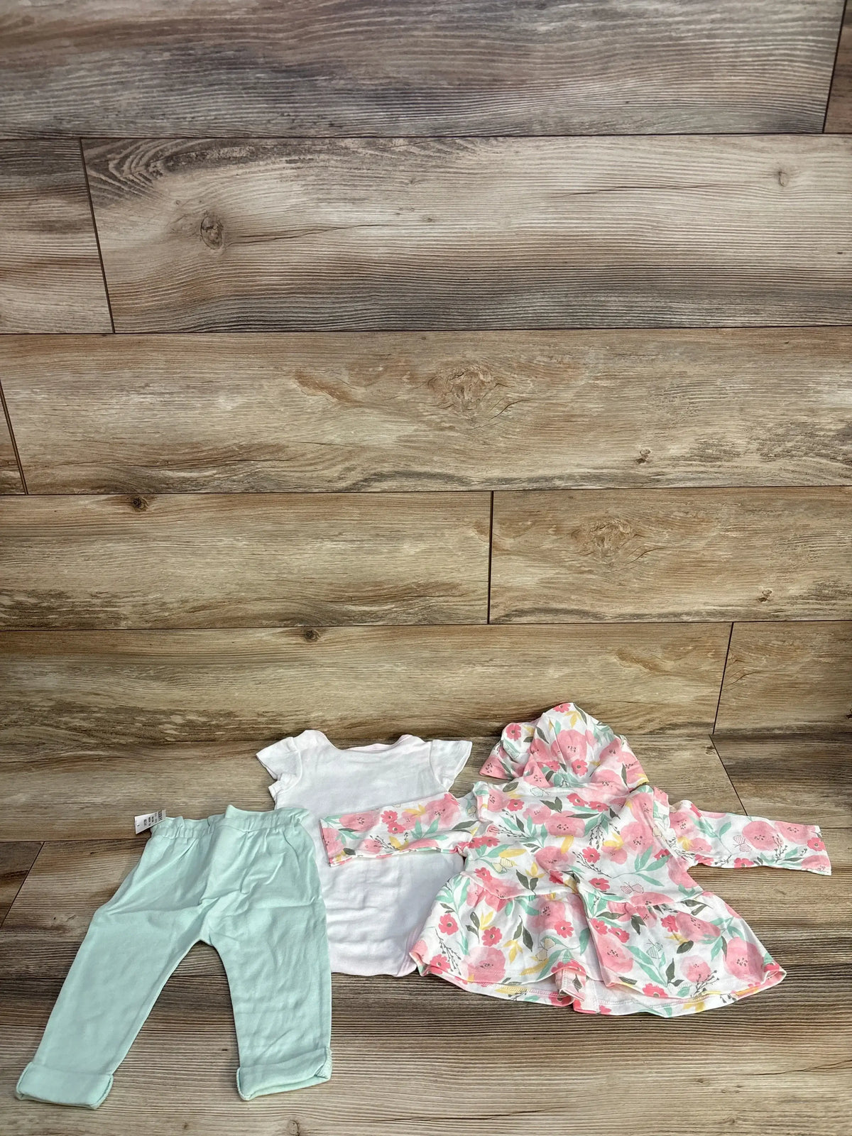 Flat lay of 3pc floral hooded jacket set (3-6M): mint leggings, white bodysuit, pink floral hooded jacket on wood floor