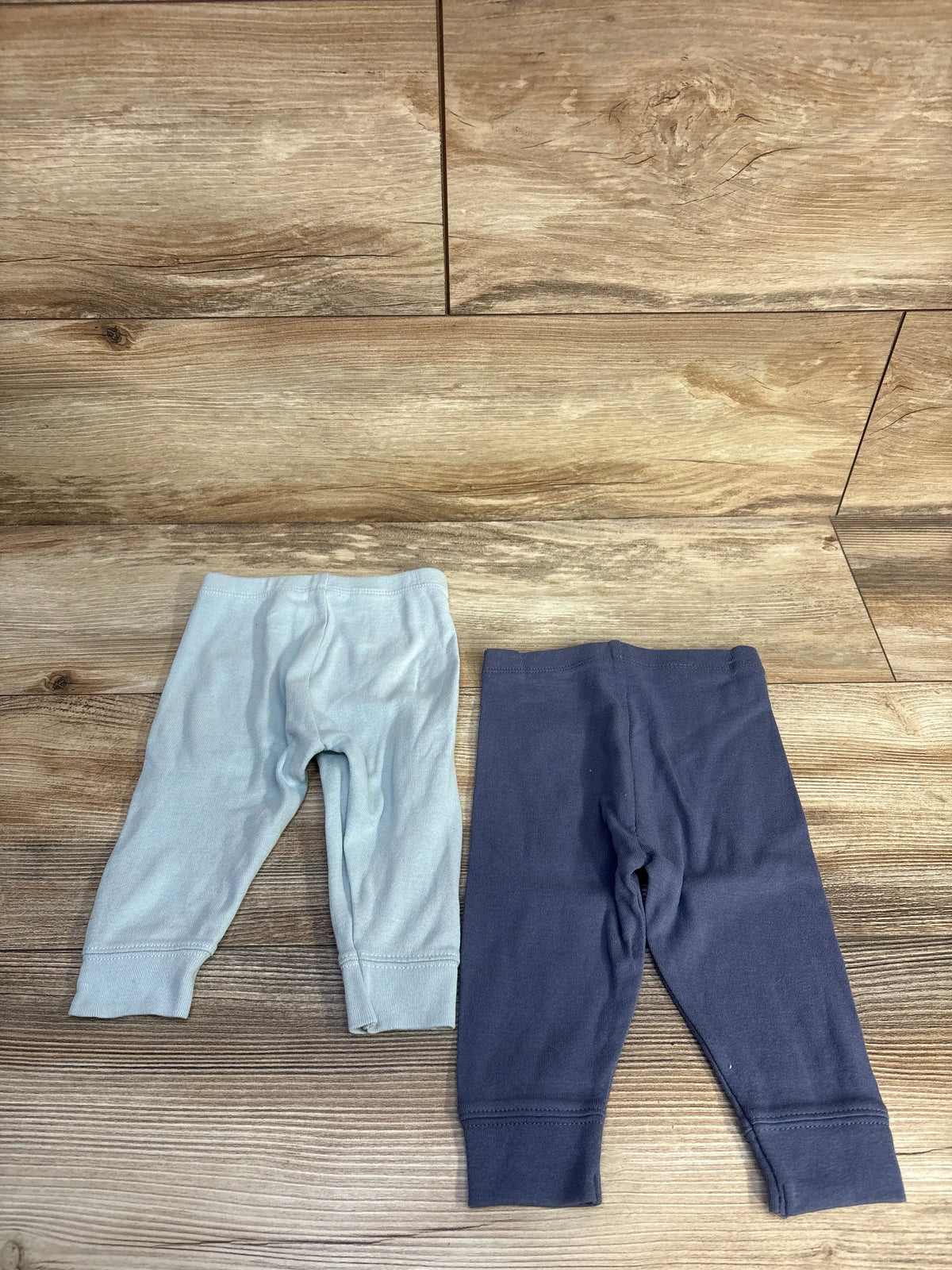 Cloud Island 2pk pull-on pants in light blue and navy blue, size 3-6m, on a wood floor.