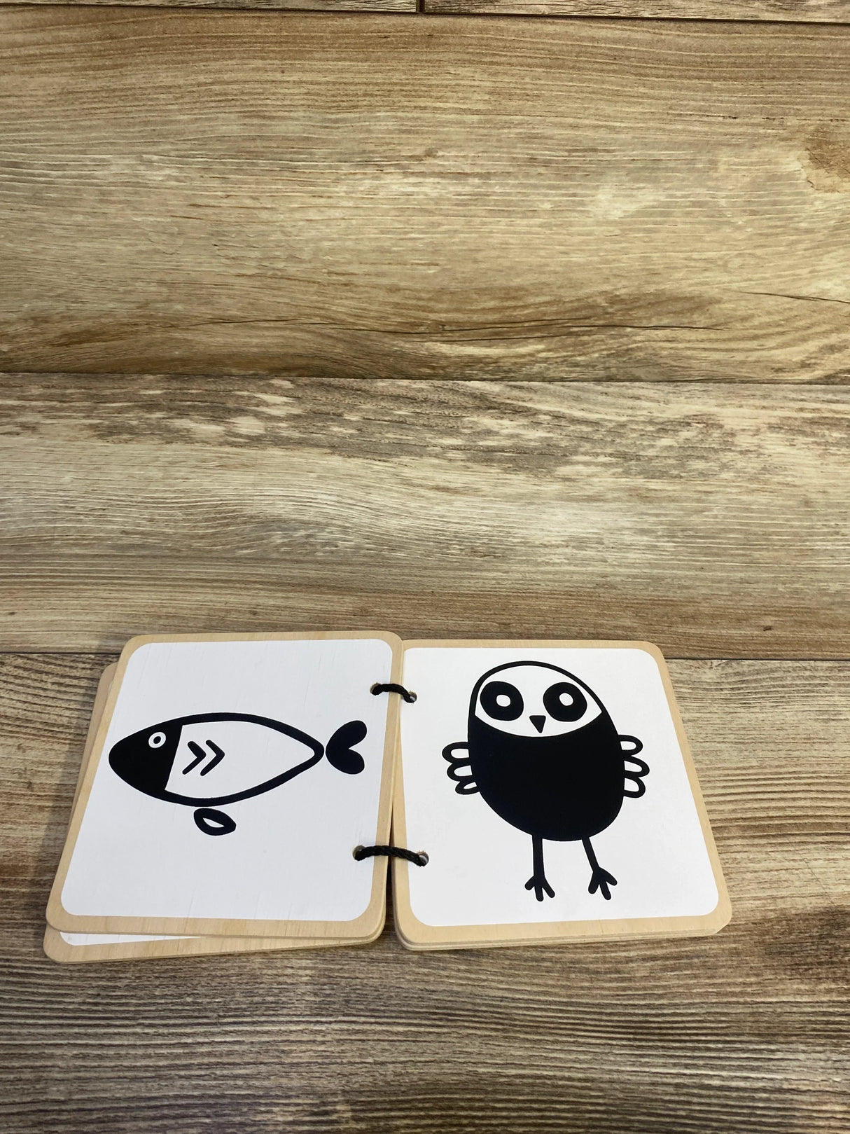 Top-down view of Lovevery wooden board book open to two high-contrast black-and-white animal cards (fish and bird) on a wood surface