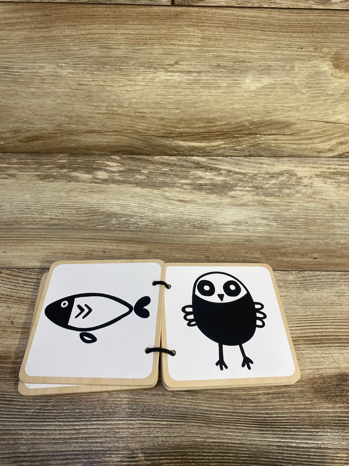 Top-down view of Lovevery wooden board book open to two high-contrast black-and-white animal cards (fish and bird) on a wood surface