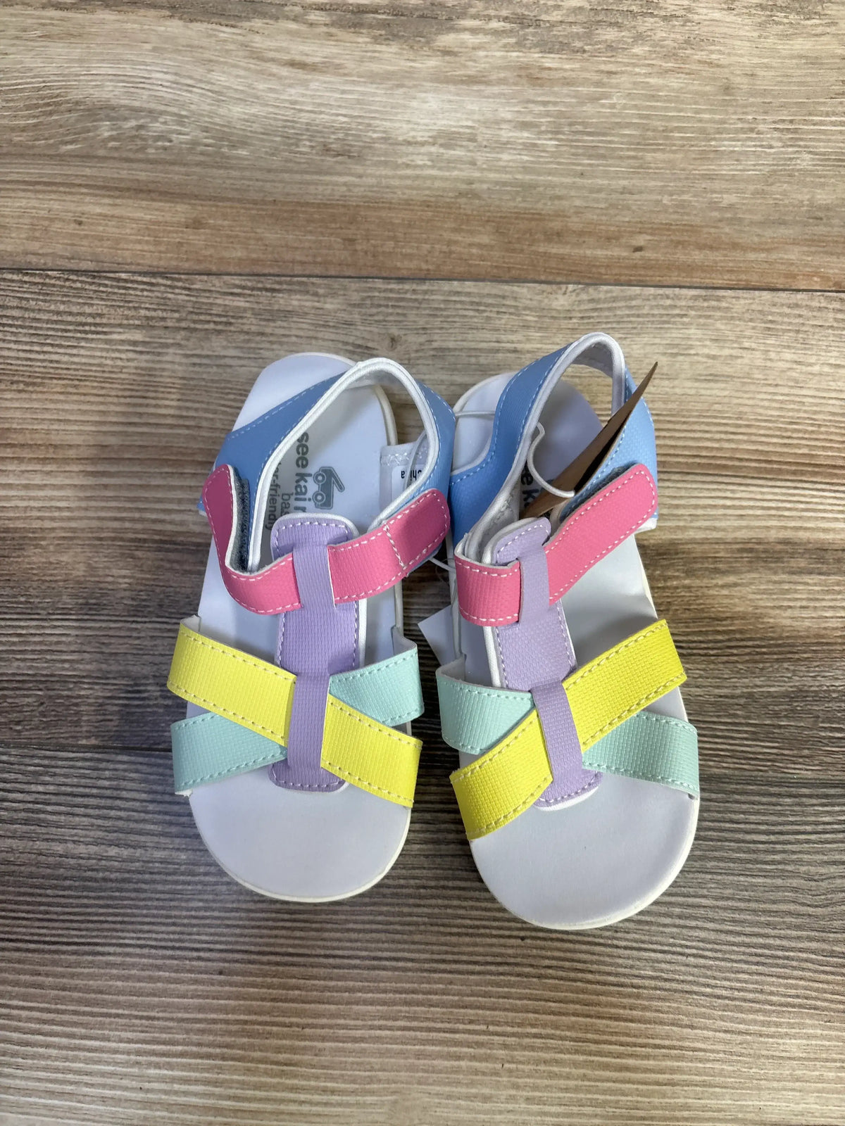 Top view of See Kai Run Shayna toddler sandals with pastel straps and Velcro ankle closures on wood floor