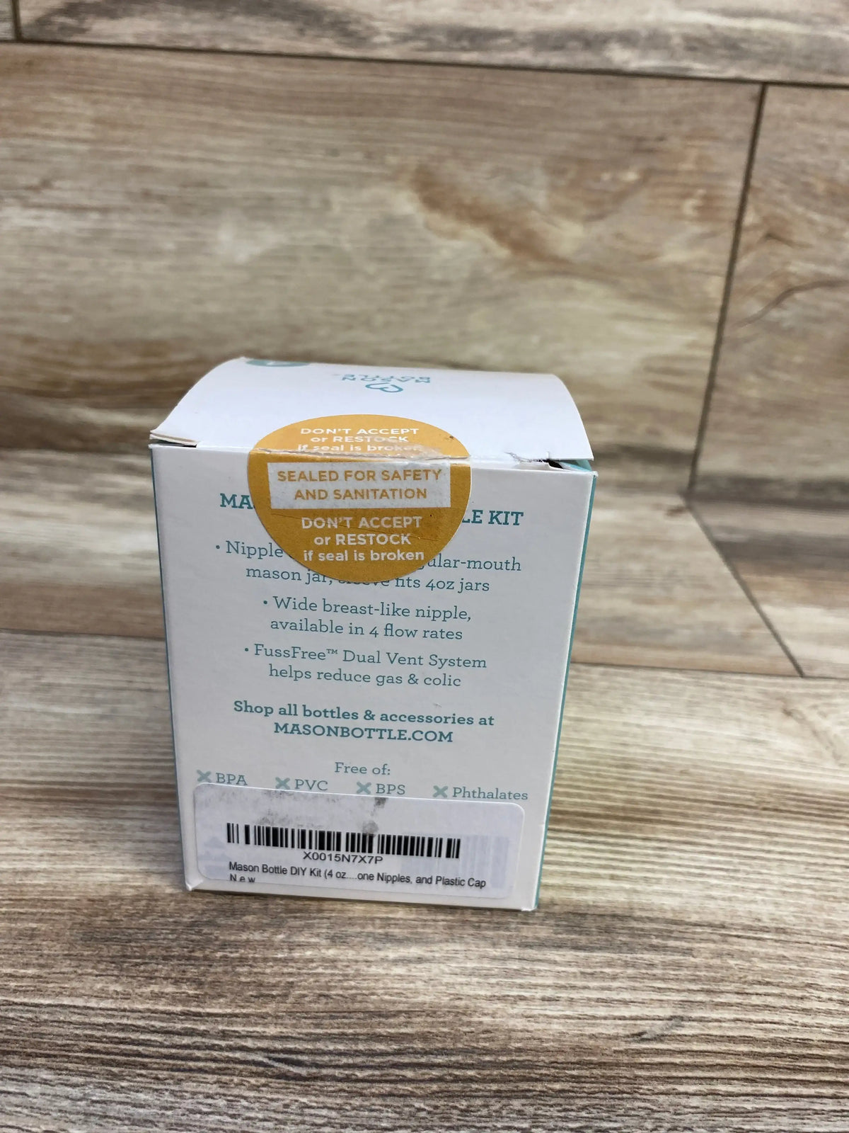 Back of New Mason Bottle glass baby bottle DIY kit 4 oz box showing sealed for safety and sanitation sticker, nipple feature text, and barcode on wood background