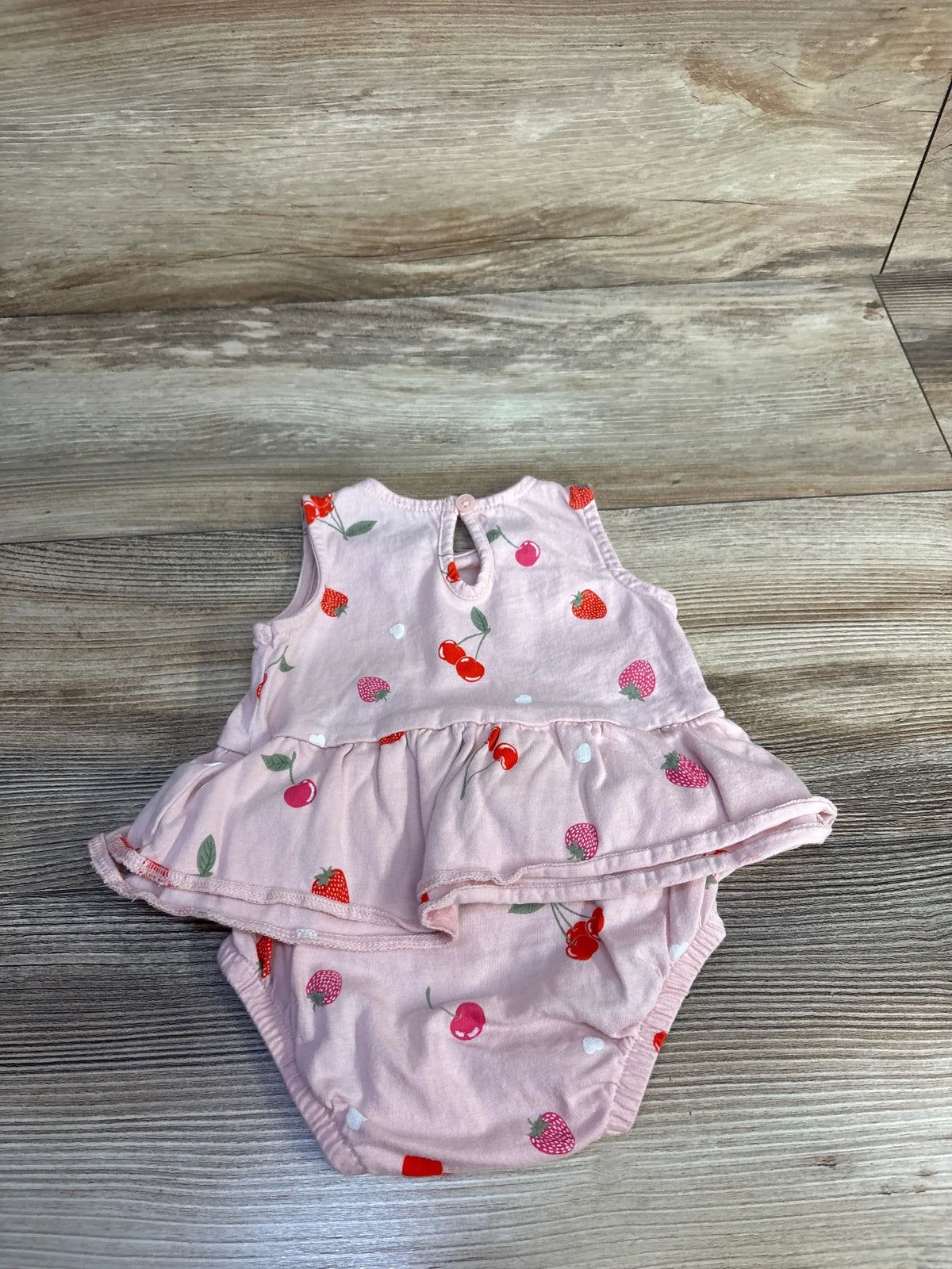 Front view of Carter’s pink bodysuit dress showcasing a fruit print and skirt overlay on a wood-grain background