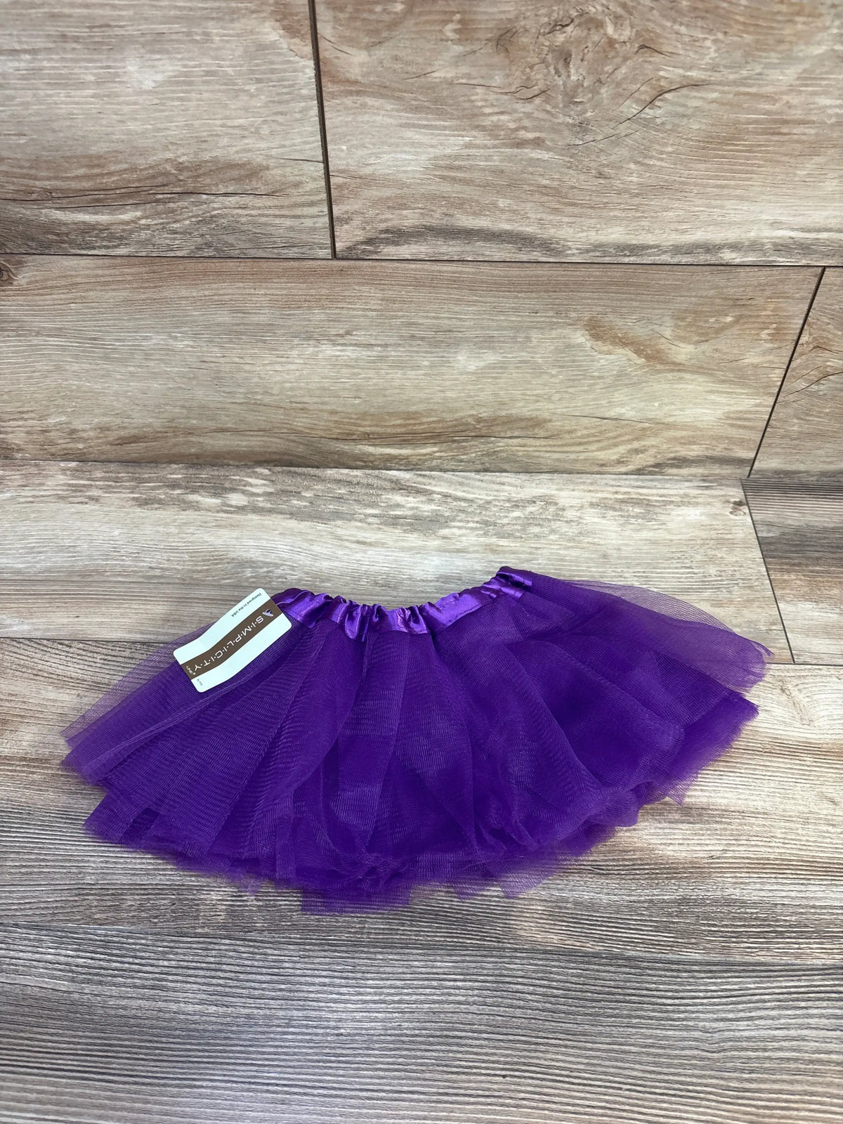 Flat lay of purple toddler tutu skirt showing layered tulle and elastic satin waistband on wood floor background