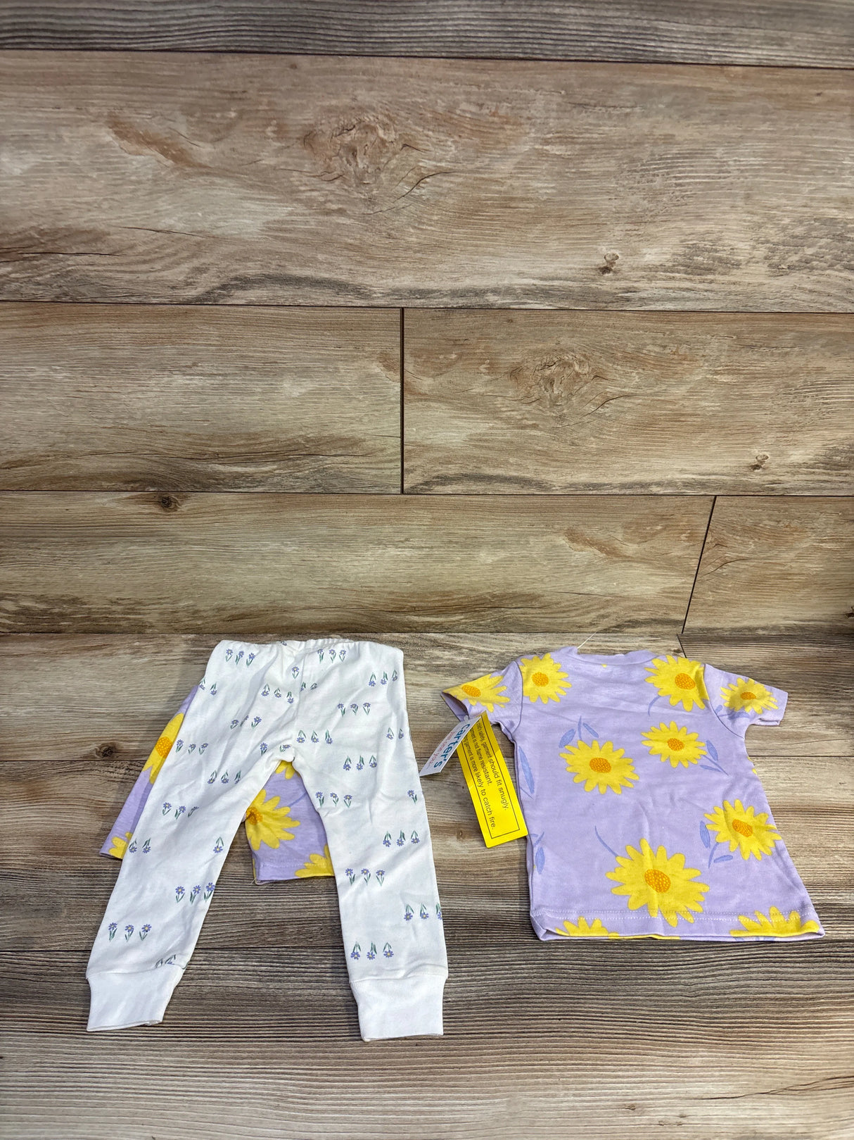 Flat lay of 3-piece infant floral pajama set: lavender tee with yellow sunflowers and white floral leggings on wood floor