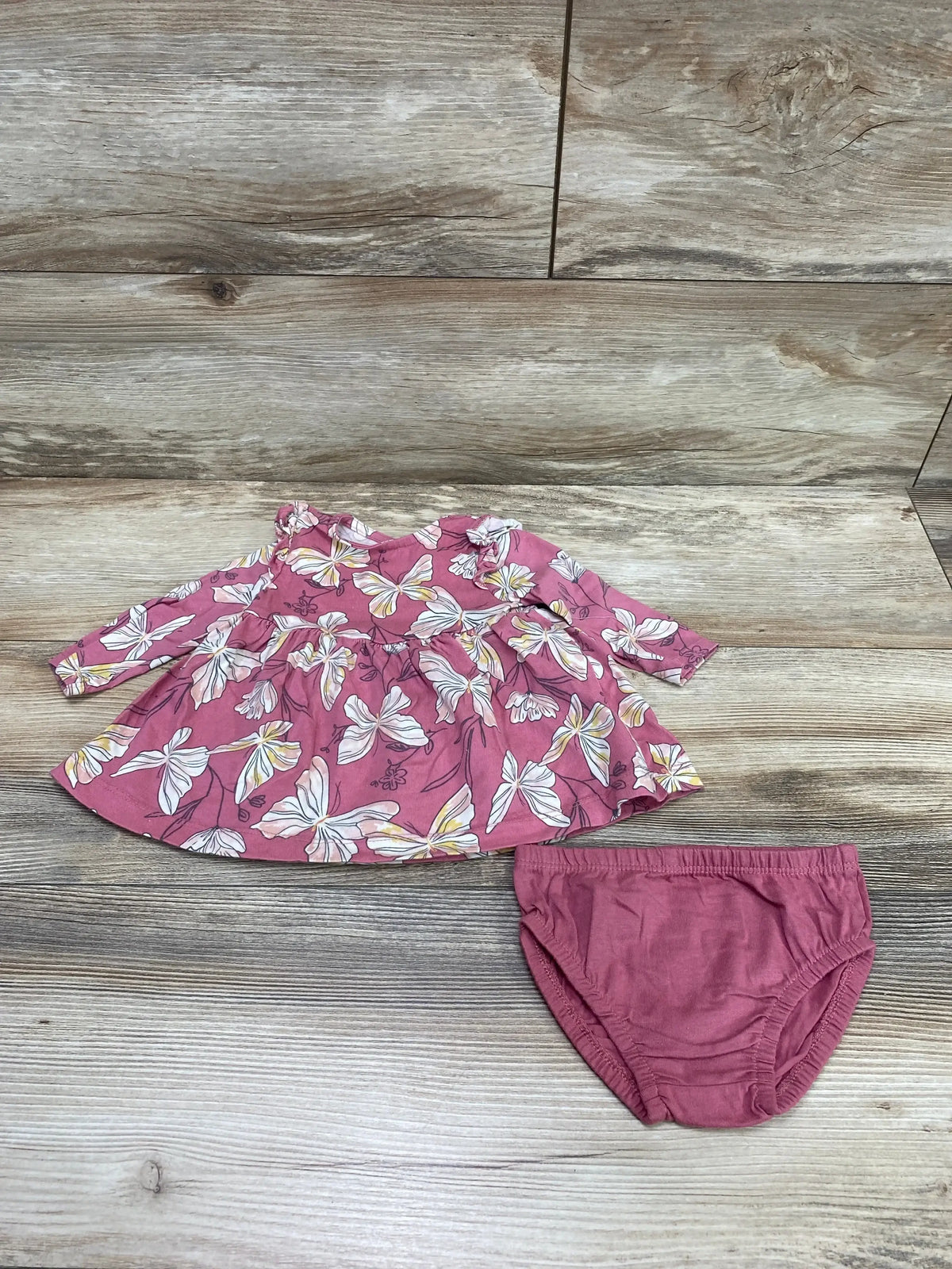 Top-down view of Carter's butterfly-print pink baby dress and matching bloomers, long sleeves and gathered skirt on wood plank background