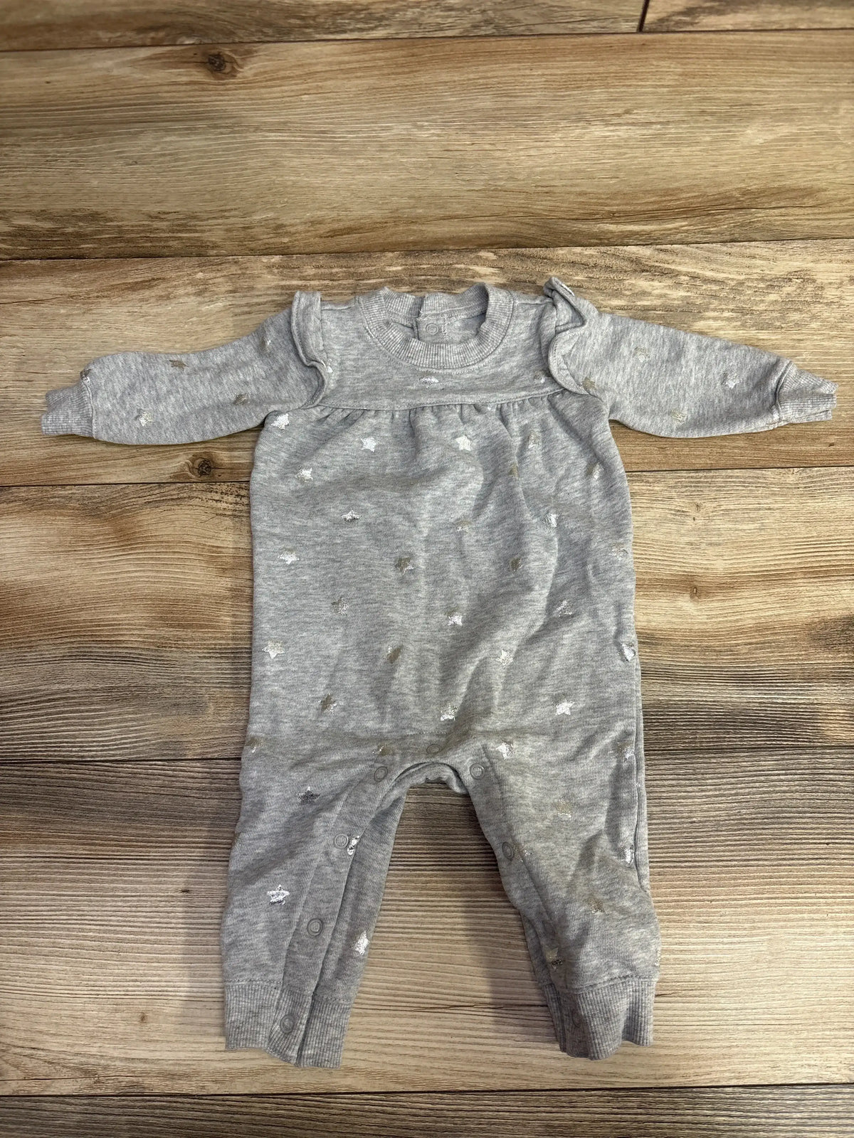 Grey baby onesie with star patterns and snap buttons on wooden floor