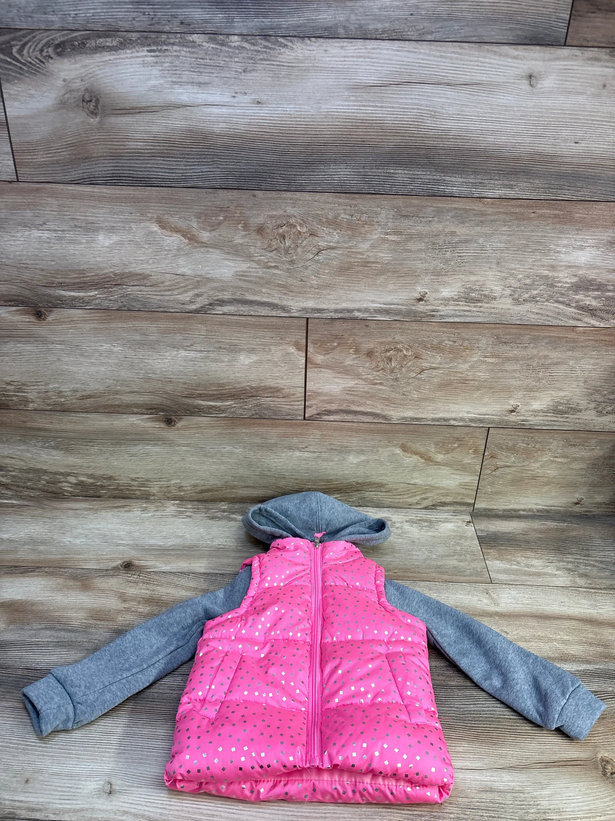 Front view of toddler pink 2fer puffer jacket with silver foil dots and attached gray hood and sleeves on wood background