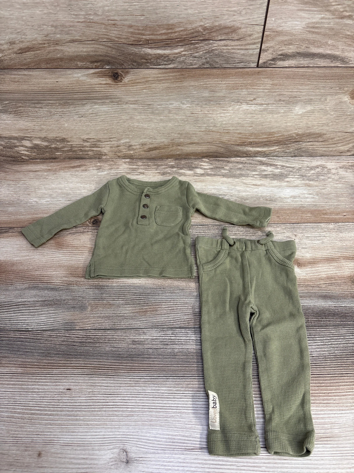 Olive green baby thermal long sleeve shirt with buttons and matching pants on wood background