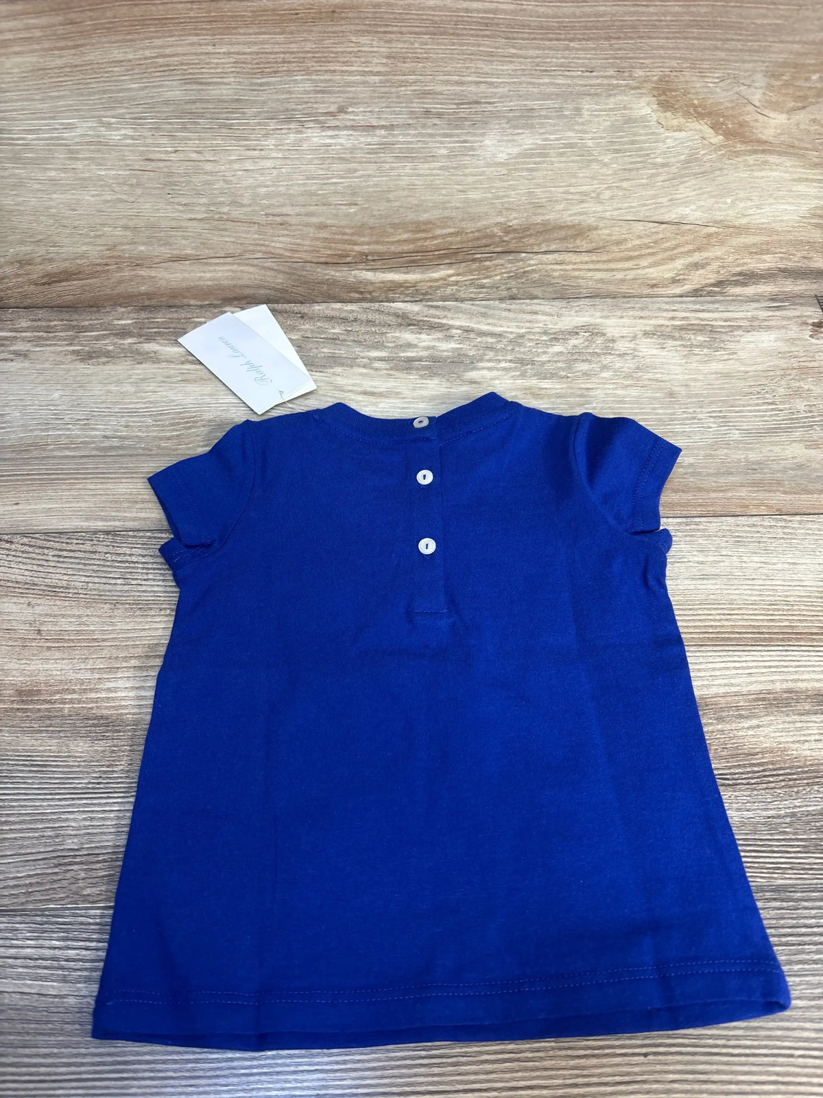 Back view of Ralph Lauren blue short-sleeve baby shirt size 9 months showcasing three white back buttons on wood surface