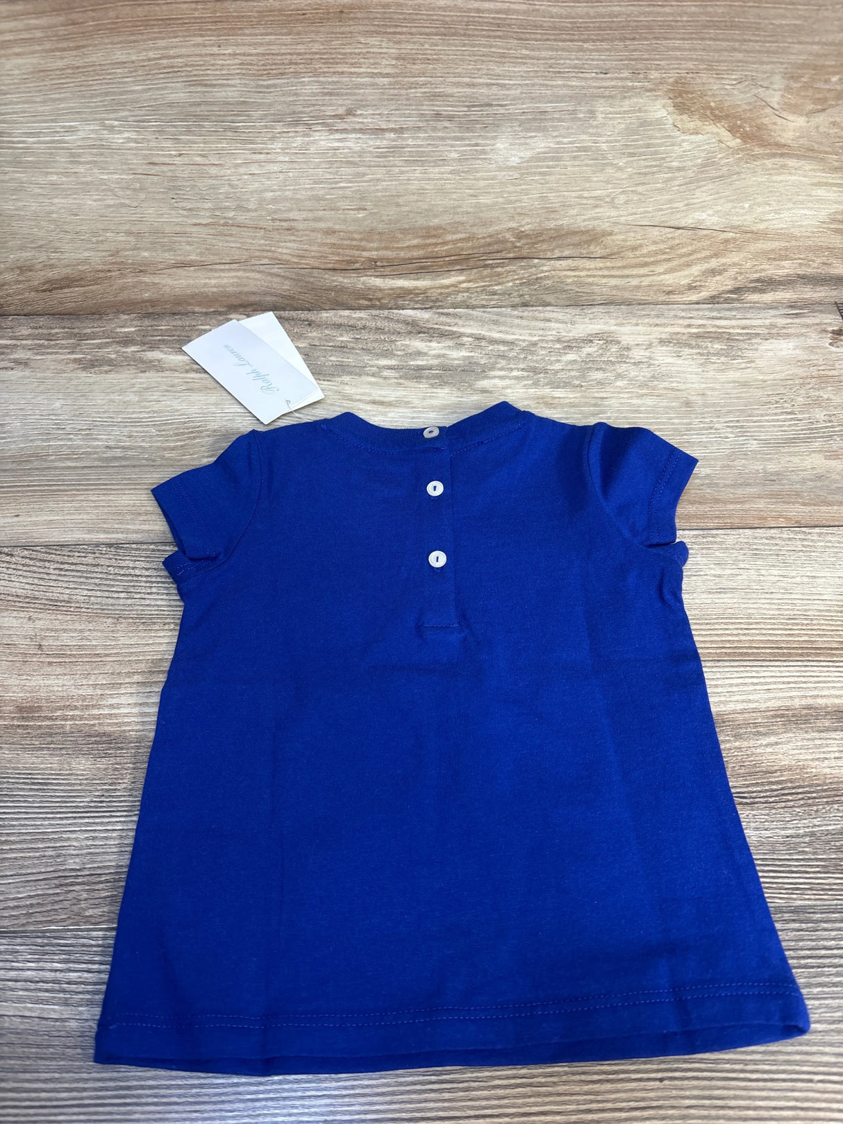 Back view of Ralph Lauren blue short-sleeve baby shirt size 9 months showcasing three white back buttons on wood surface