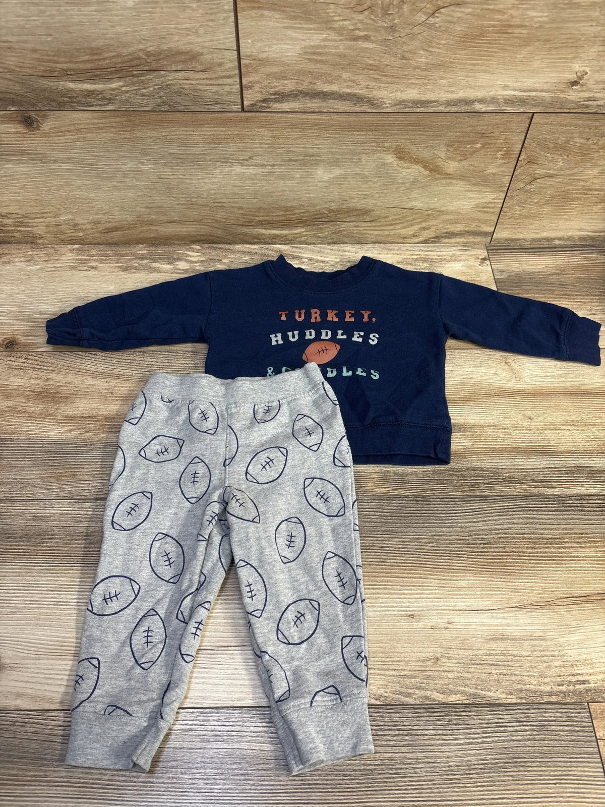 Front view of navy football sweatshirt with graphic text and gray football print pants on a wood floor