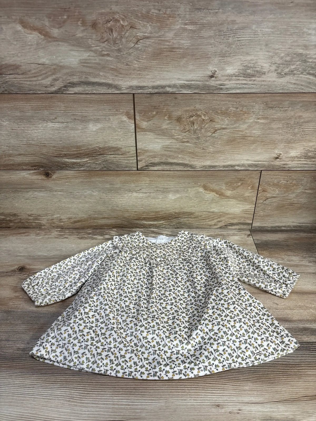 Front view of Mayoral newborn long sleeve dress in cream with small ditsy floral print and full skirt on wood plank floor