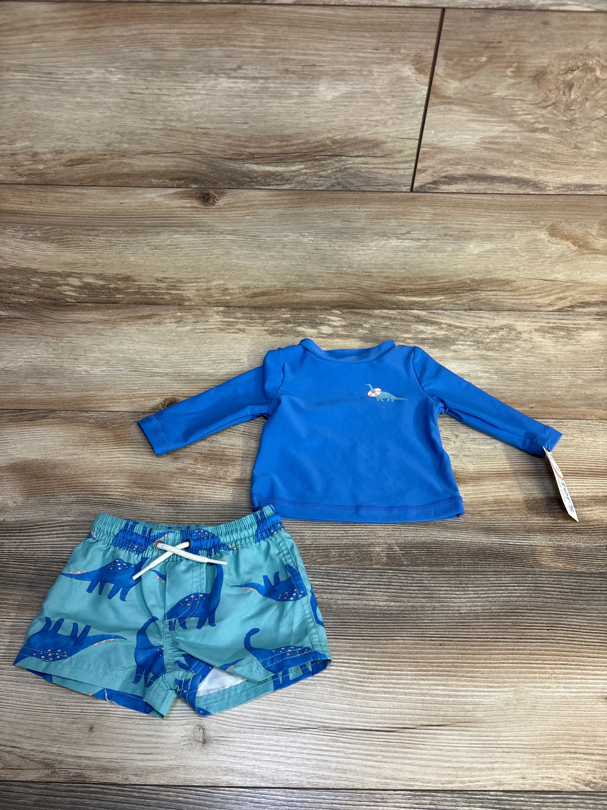 Blue dinosaur print toddler swim set with long-sleeve rash guard and swim trunks on wood floor