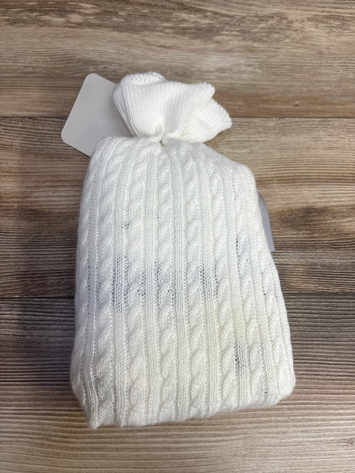 Folded view of Dream Big Little One swaddle blanket in white showcasing cable knit texture and knotted top on wood background