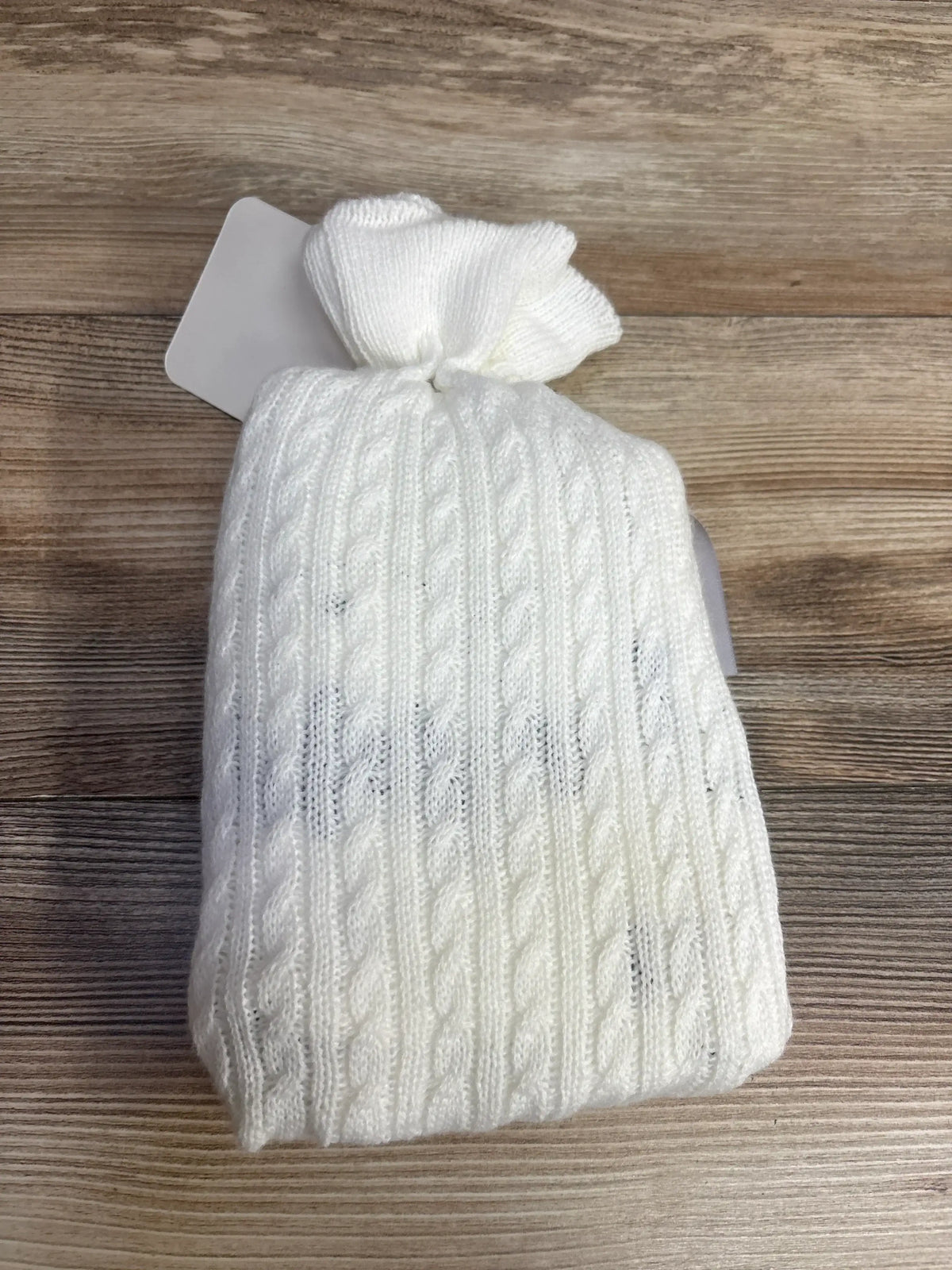 Folded white Dream Big Little One swaddle blanket showcasing cable knit texture and knotted top on wood background