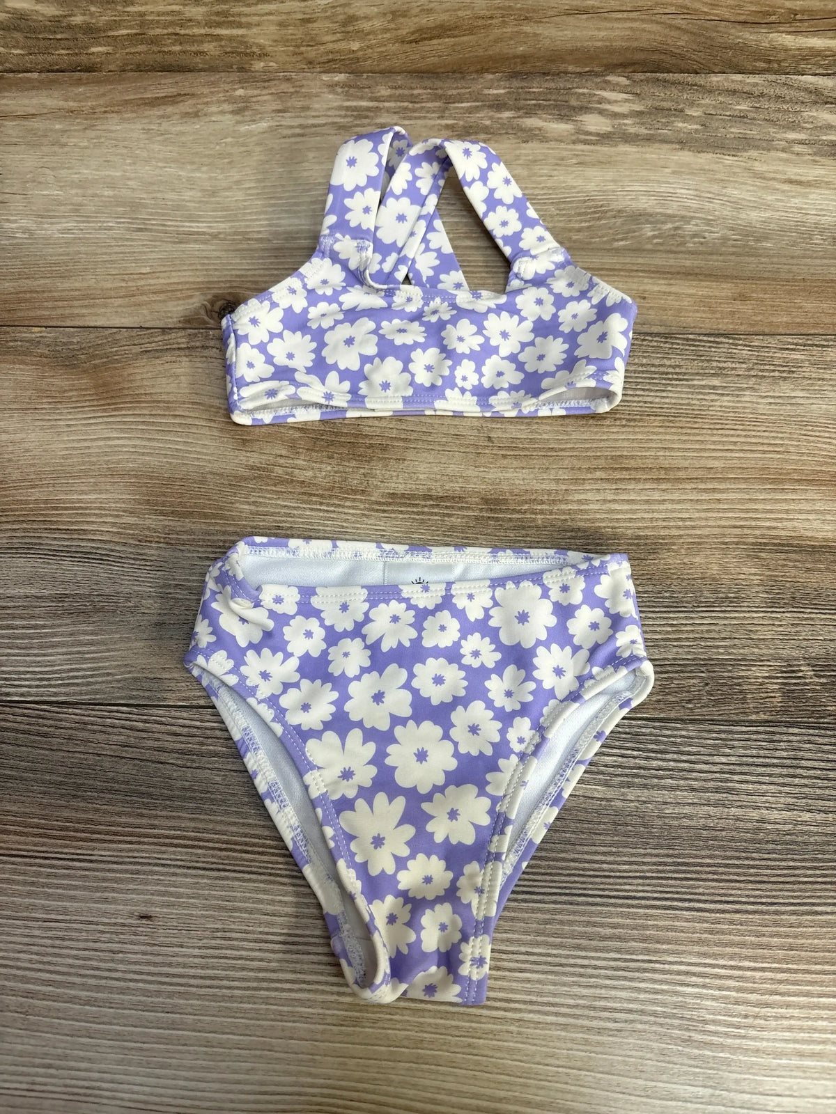Flat lay of purple two-piece floral baby swimsuit showing high-rise bottoms and racerback top on wood background