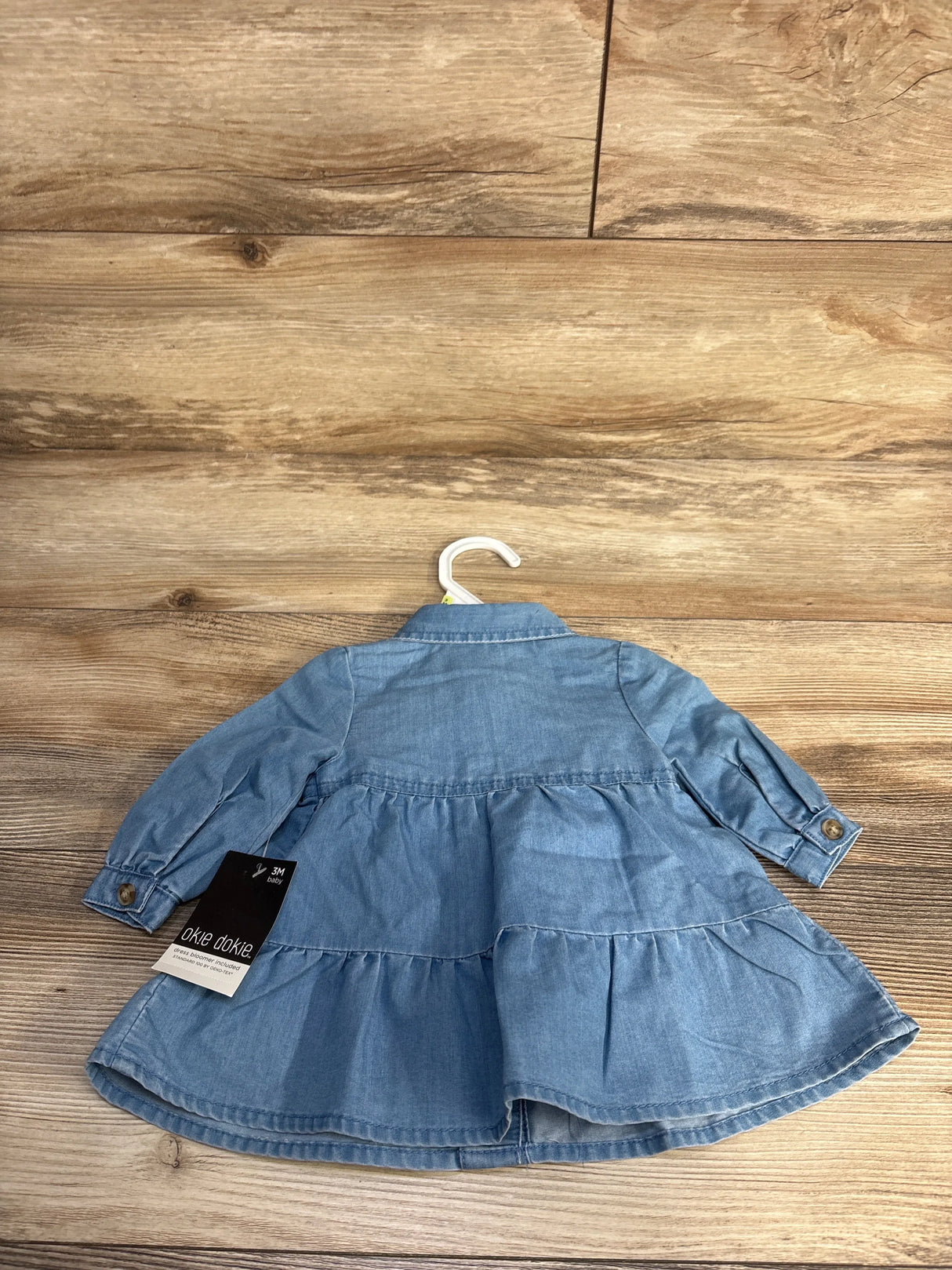 Light blue denim baby dress with long sleeves and a collar, displayed on wooden floor