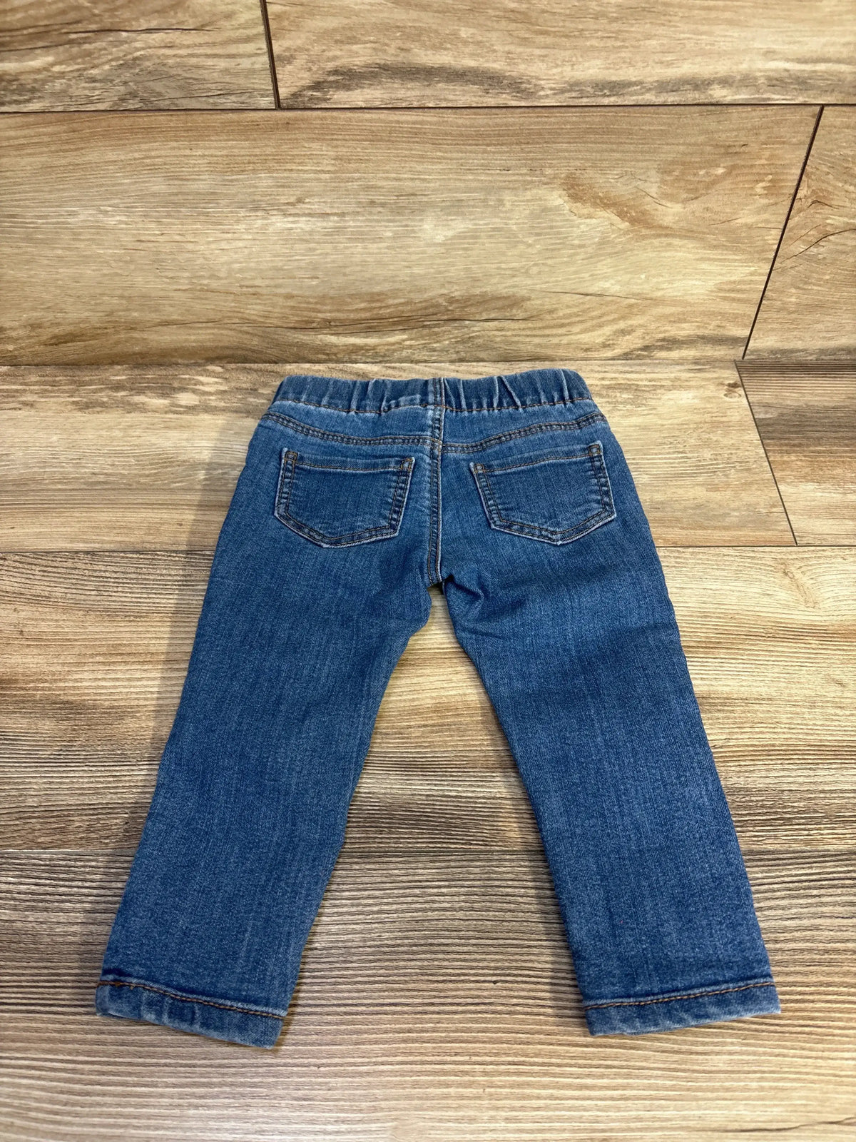 Back view of blue Oshkosh toddler jeggings (18 months) showcasing elastic waistband, back patch pockets, and straight legs on light wood floor