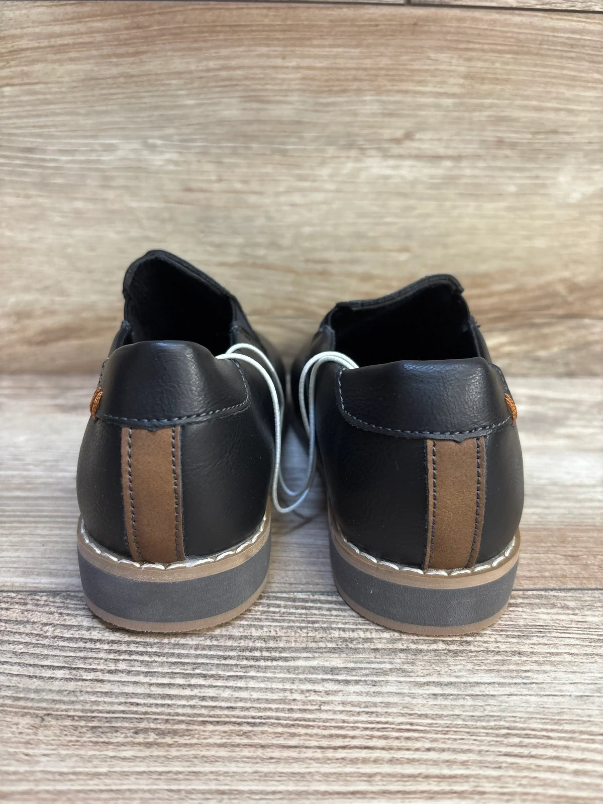 Back view of NWOT Cat and Jack Neal loafers sz 11c showcasing black faux leather with brown suede heel stripe on wood plank floor