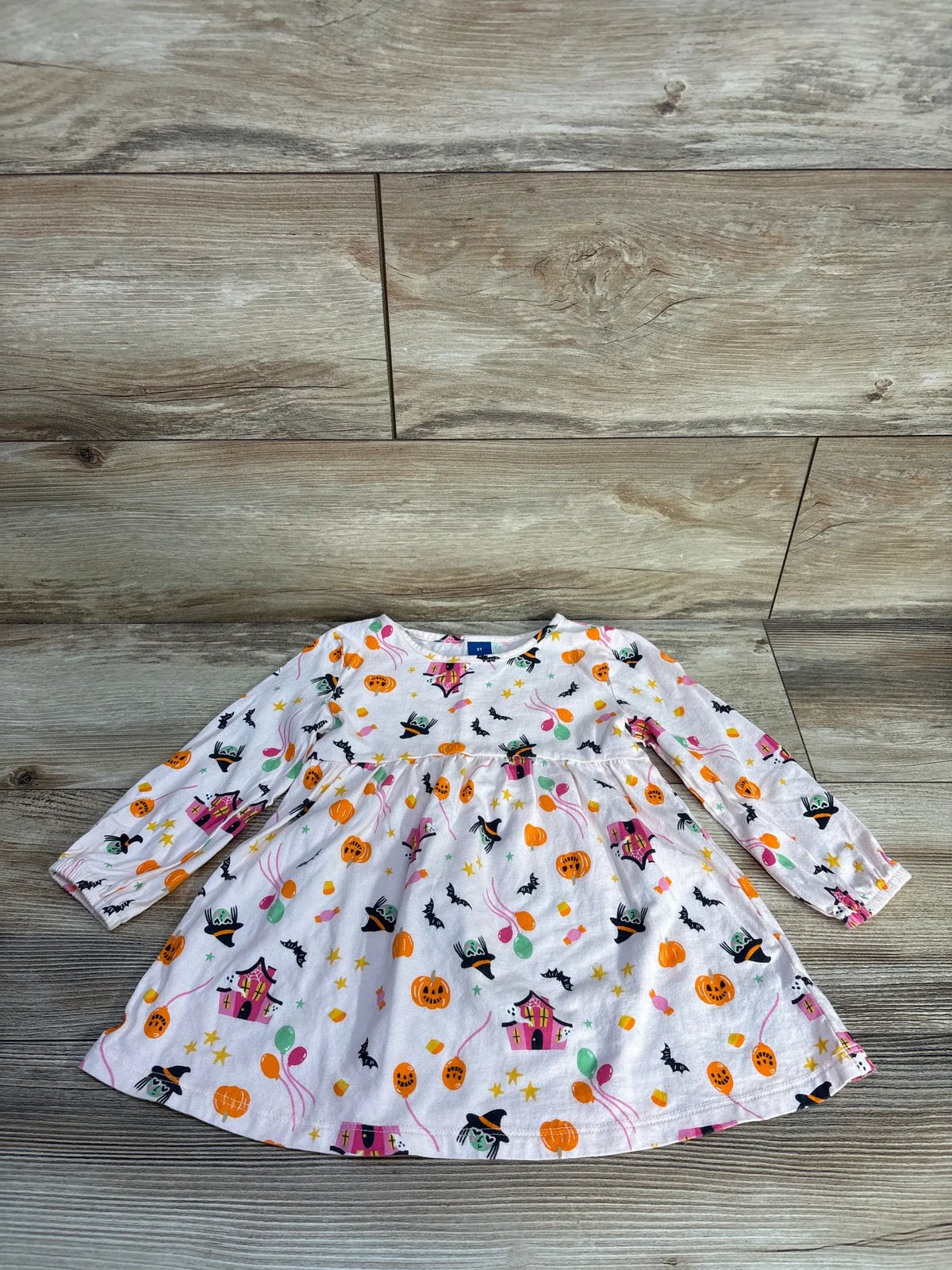 Front view of Old Navy pink Halloween icon long sleeve dress showcasing puffy sleeves, seamed waist, and all-over print on wood background