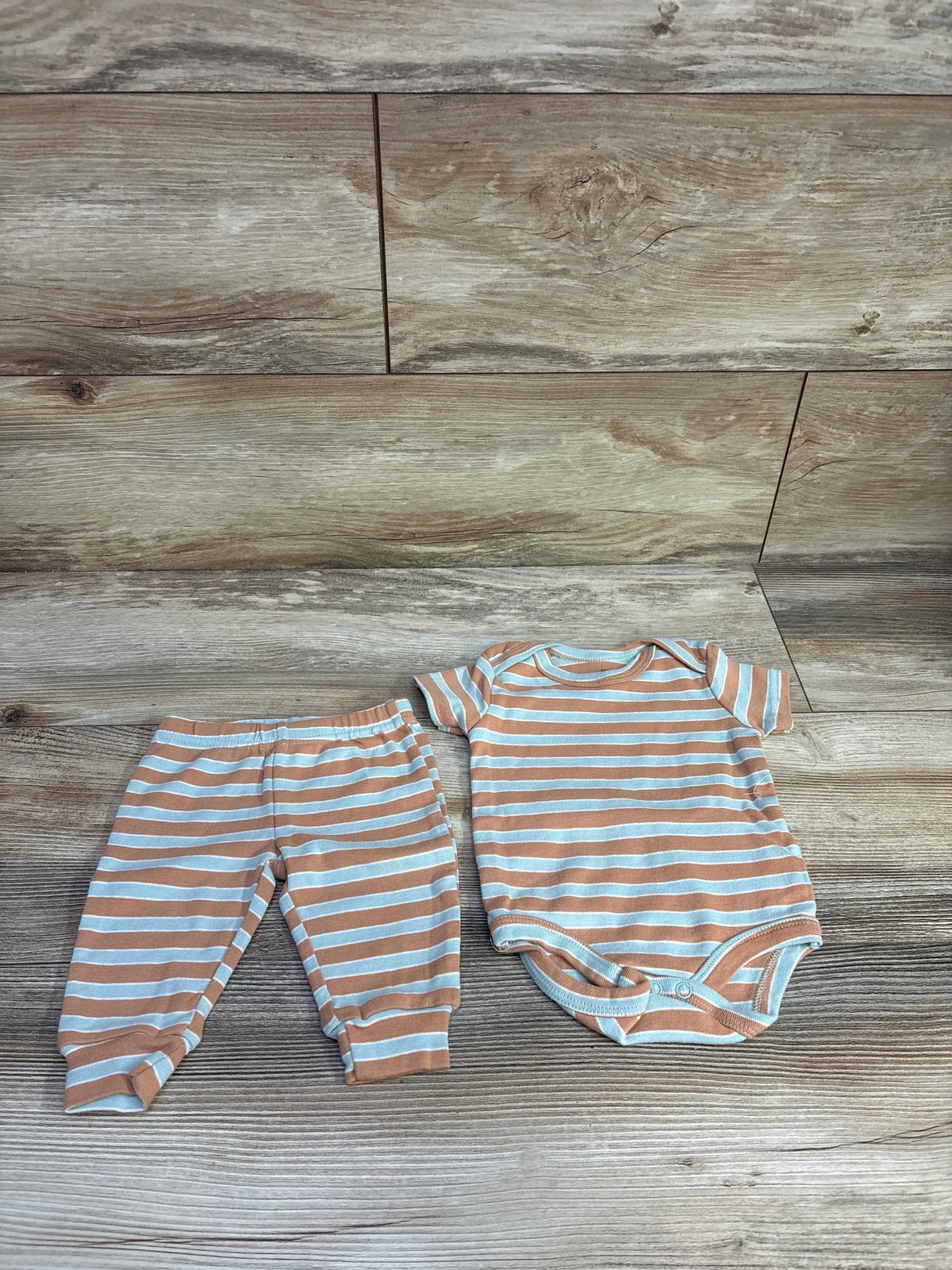 Flat lay of brown and white striped baby bodysuit and matching pants showing short sleeves and snap crotch on wood background