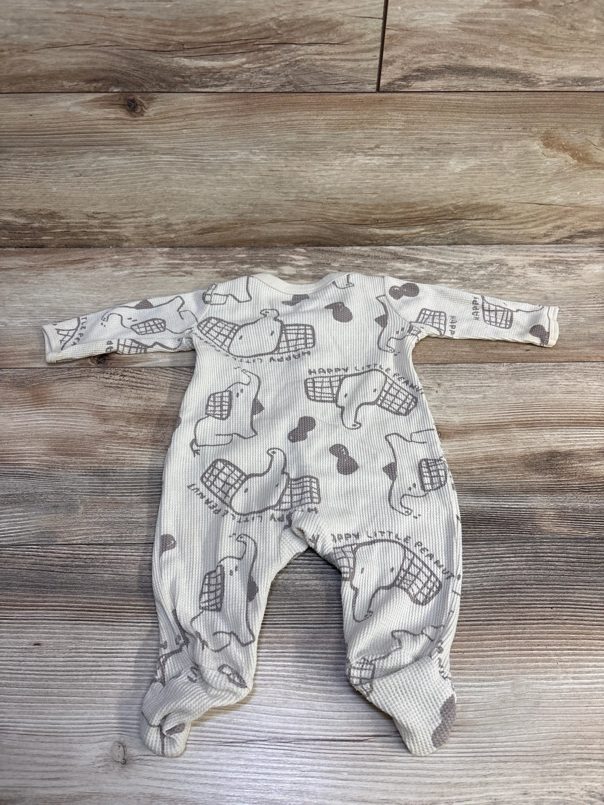Front view of Carter’s beige waffle knit snap sleeper showcasing elephant print and footed legs on a wood floor