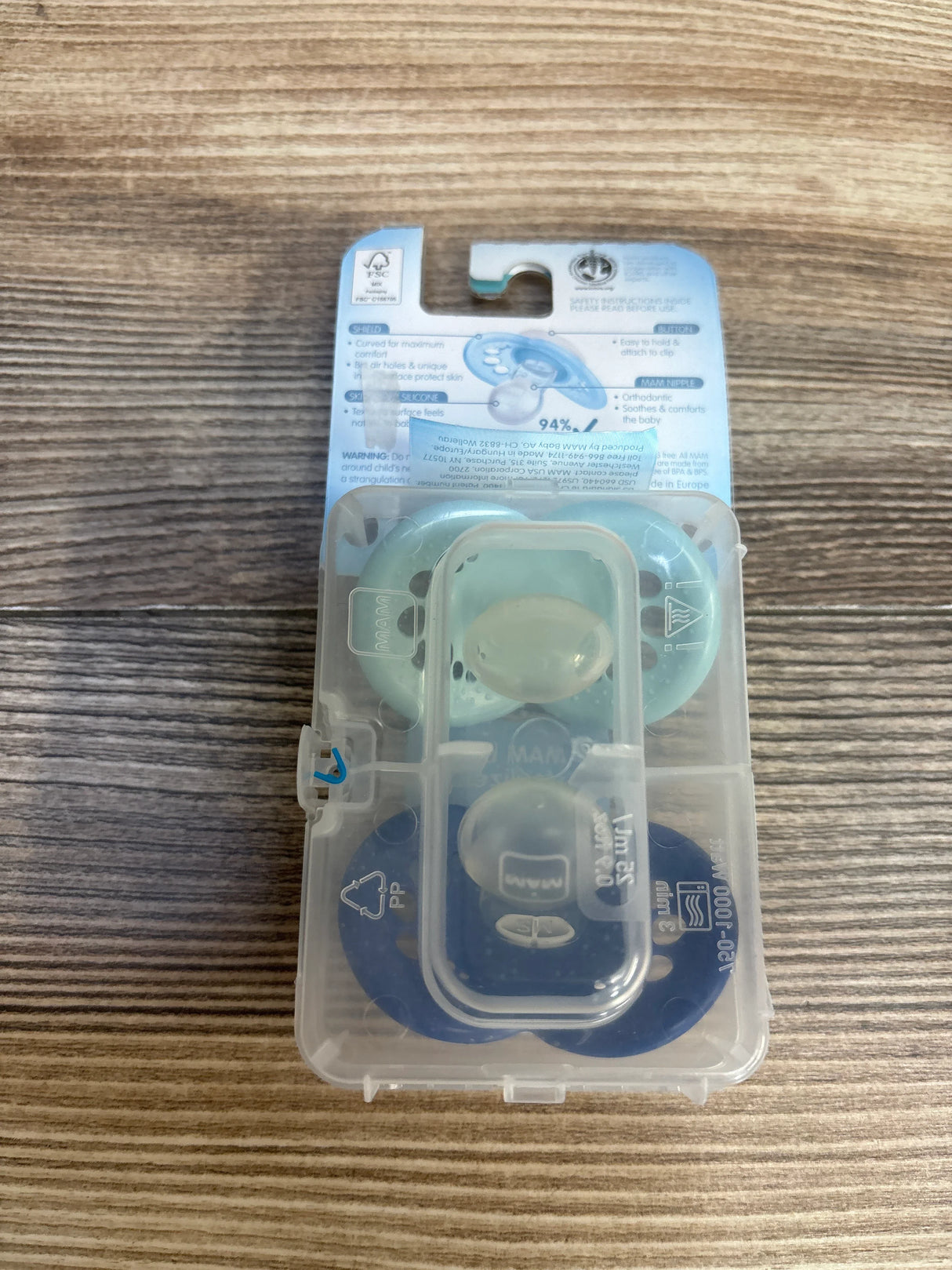 Two baby pacifiers in blue and green case on wood background