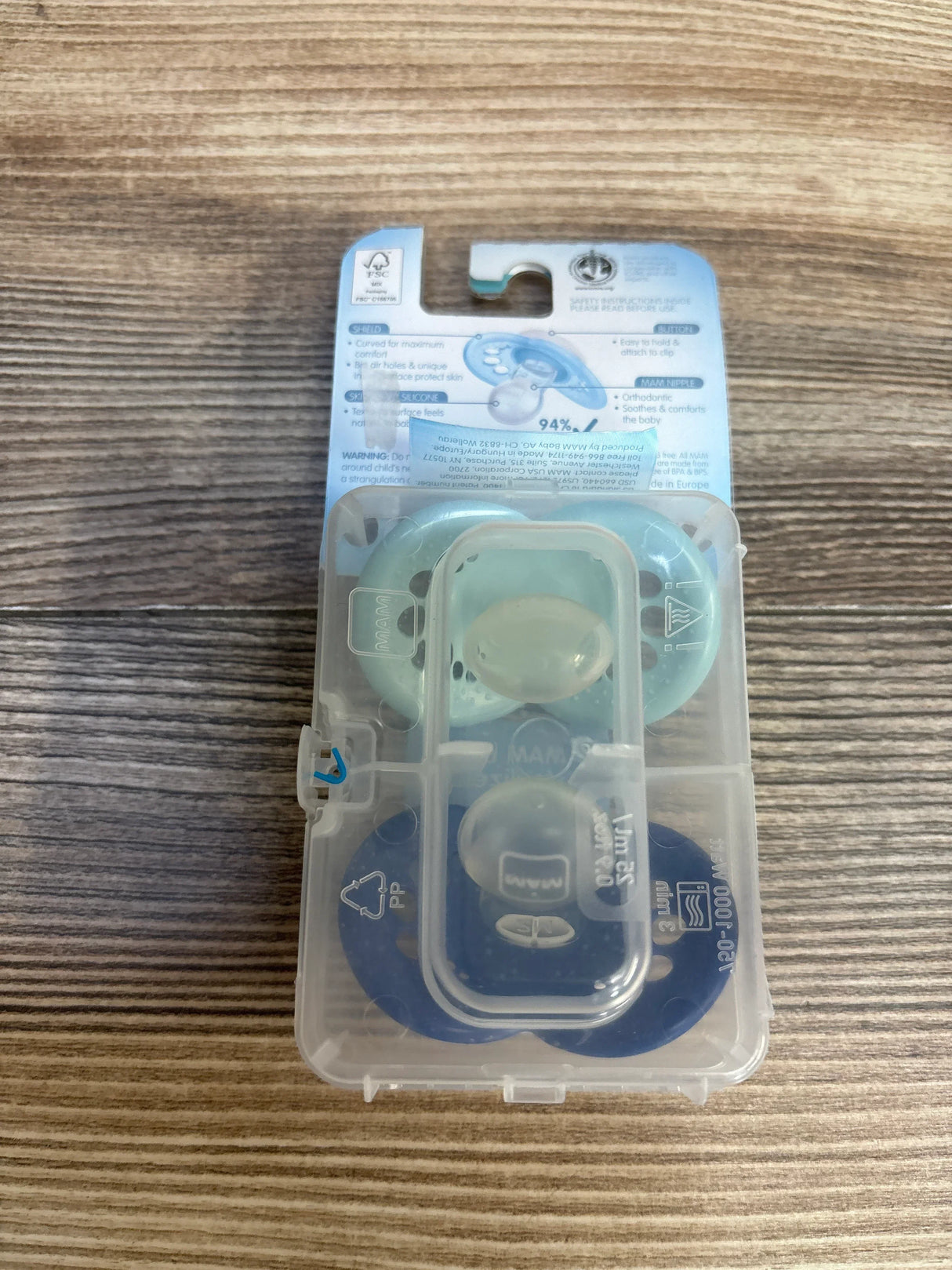 Flat lay of NEW MAM Original 2 pack pacifiers 16m plus in mint and navy in sealed original packaging on wood plank floor