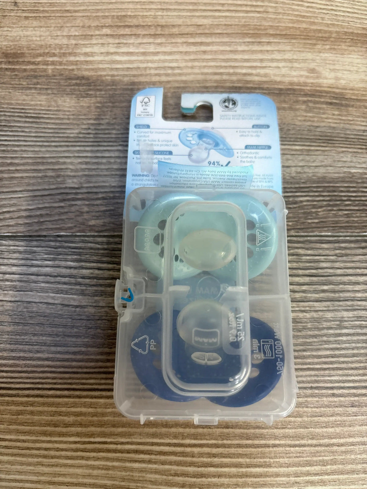 Flat lay of NEW MAM Original 2-pack pacifiers showing mint and navy pacifiers in sealed sterilizing case on wood surface