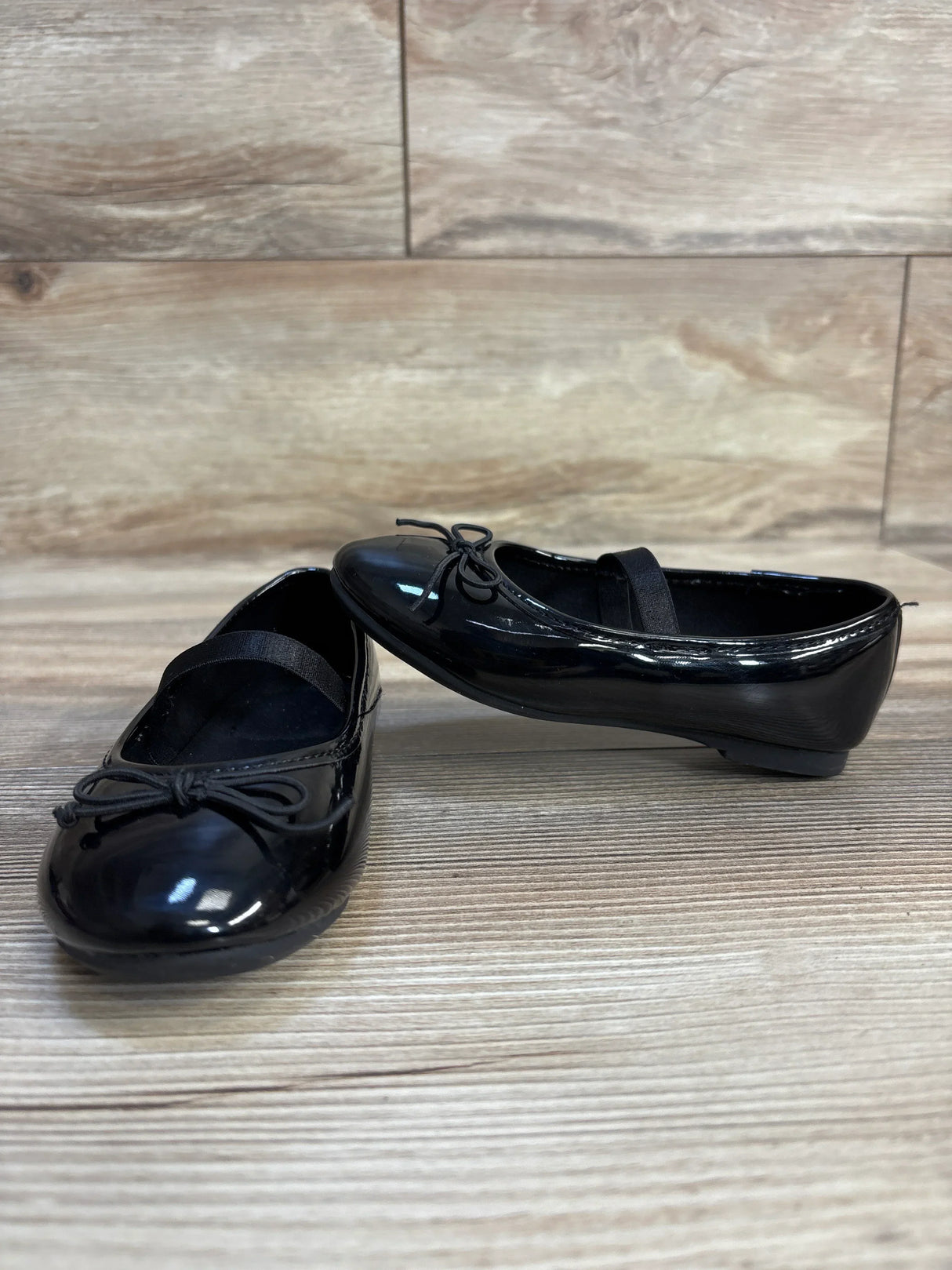 Black patent leather toddler dress shoes with bow detail on wood floor
