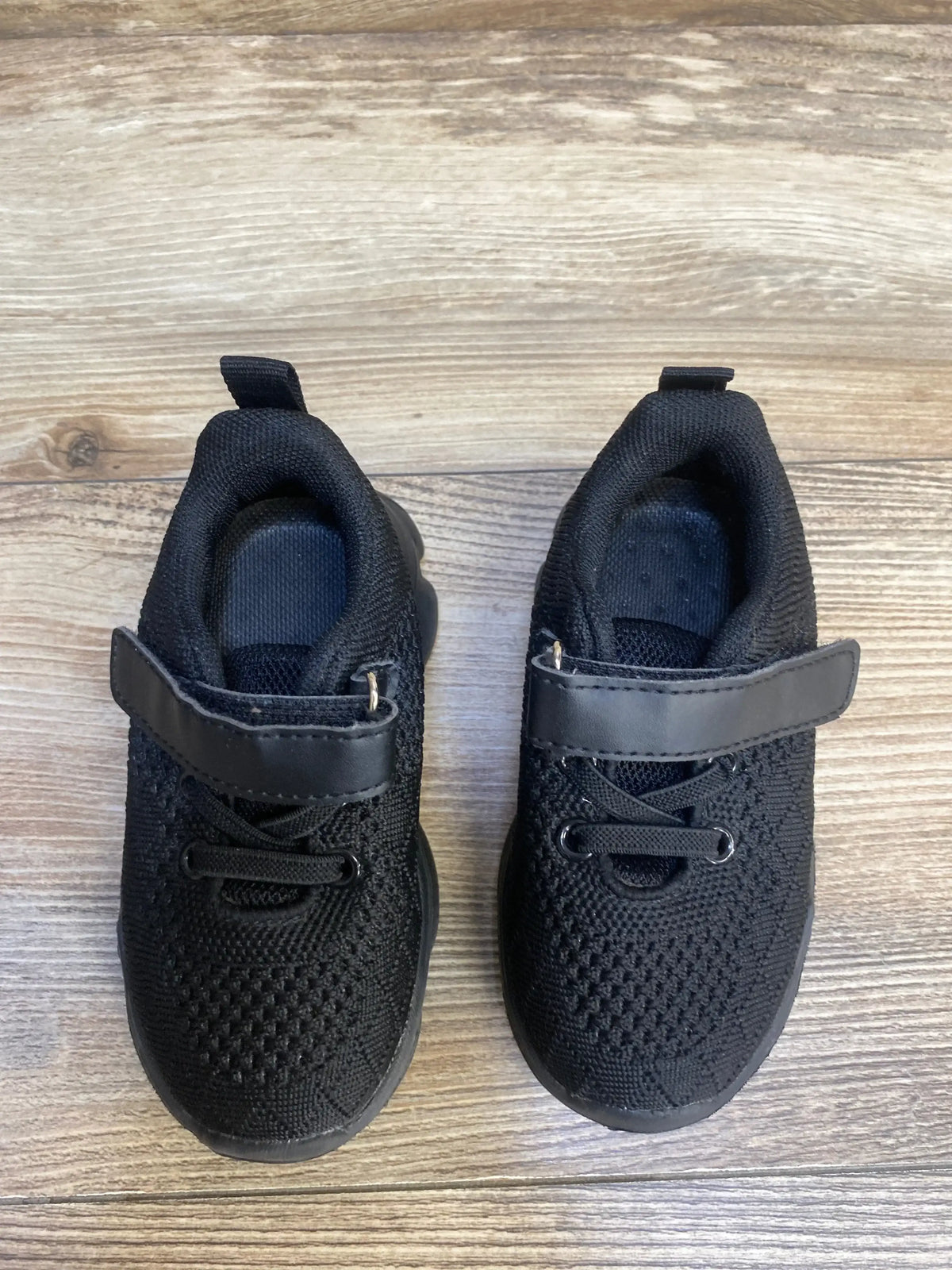 Black toddler sneakers with velcro straps and mesh fabric on wood floor