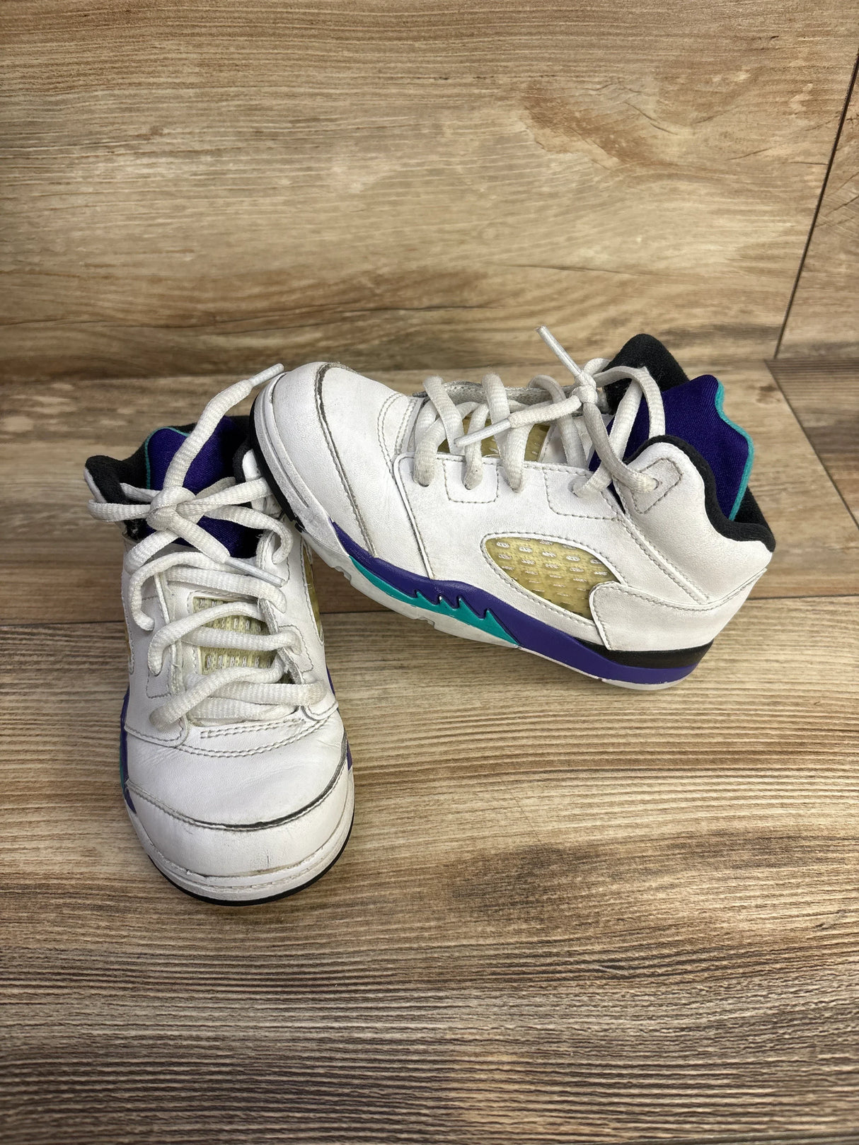 Three-quarter view of Air Jordan 5 Retro TD Grape sneakers size 10c showcasing white leather with purple and teal accents on wood plank floor