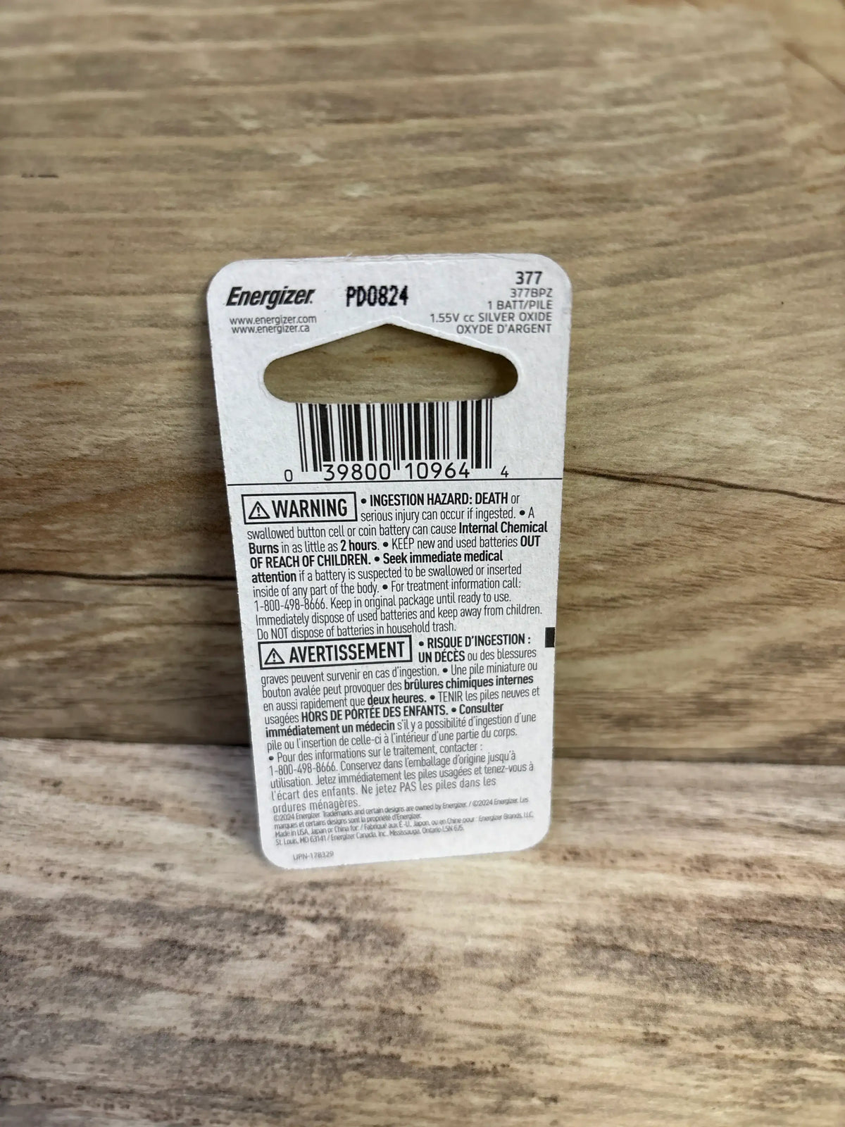 Back view of Energizer 377 button battery packaging showing barcode, warning text, and hang tab on wooden surface
