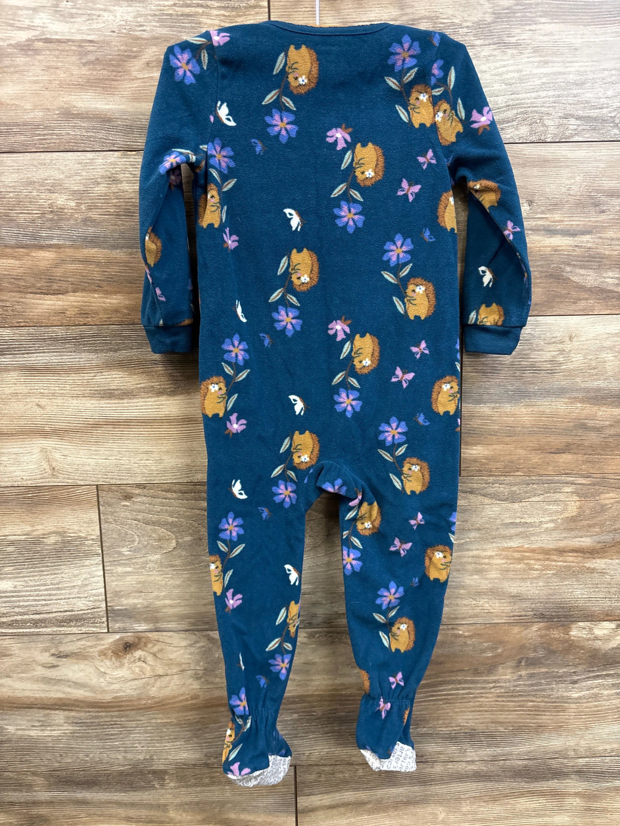 Back view of blue Carter’s footed blanket sleeper showing hedgehog and purple flower print on wood background
