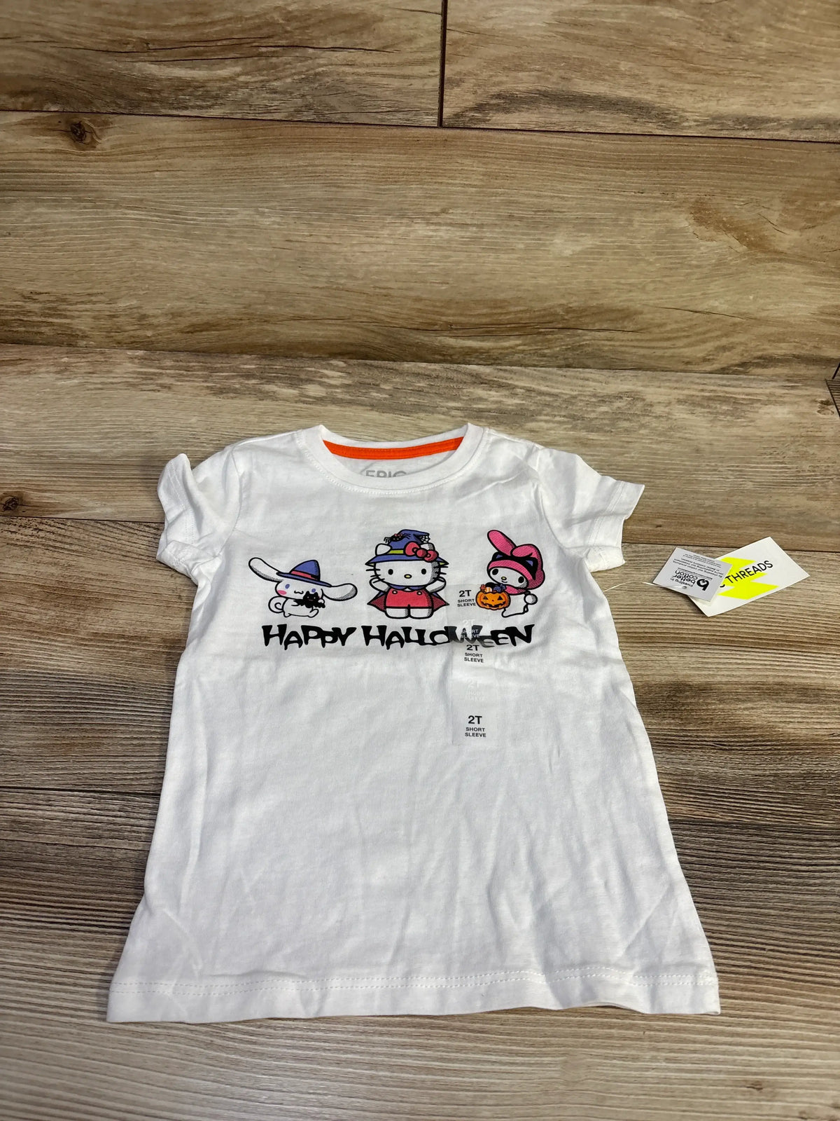 Front flat lay of Epic Threads x Hello Kitty white toddler T-shirt 2T with Halloween character graphic and Happy Halloween text on wood floor