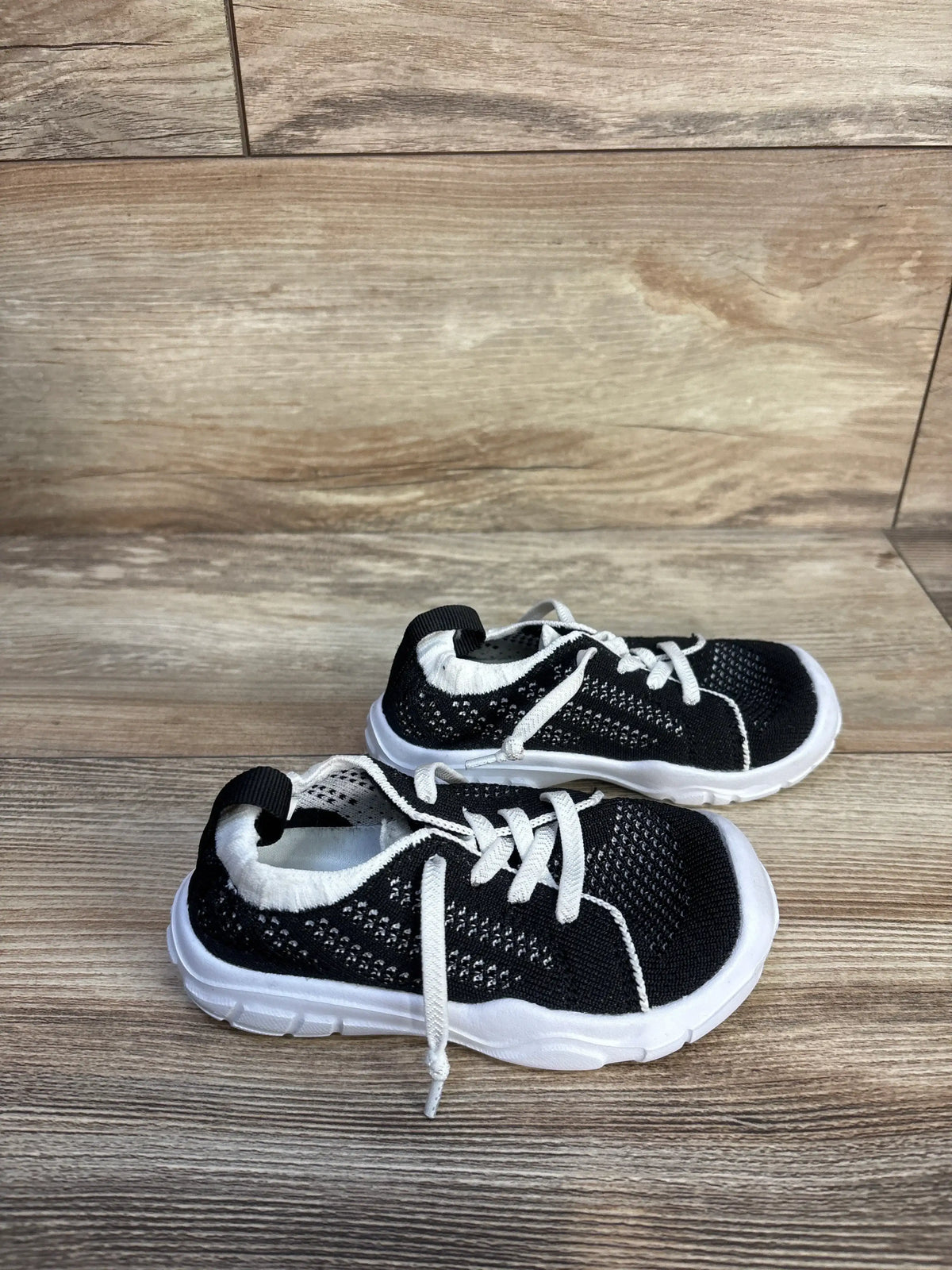 Close-up of Eqw slip-on sneakers in black, showcasing white soles and knit uppers on a wood-look floor