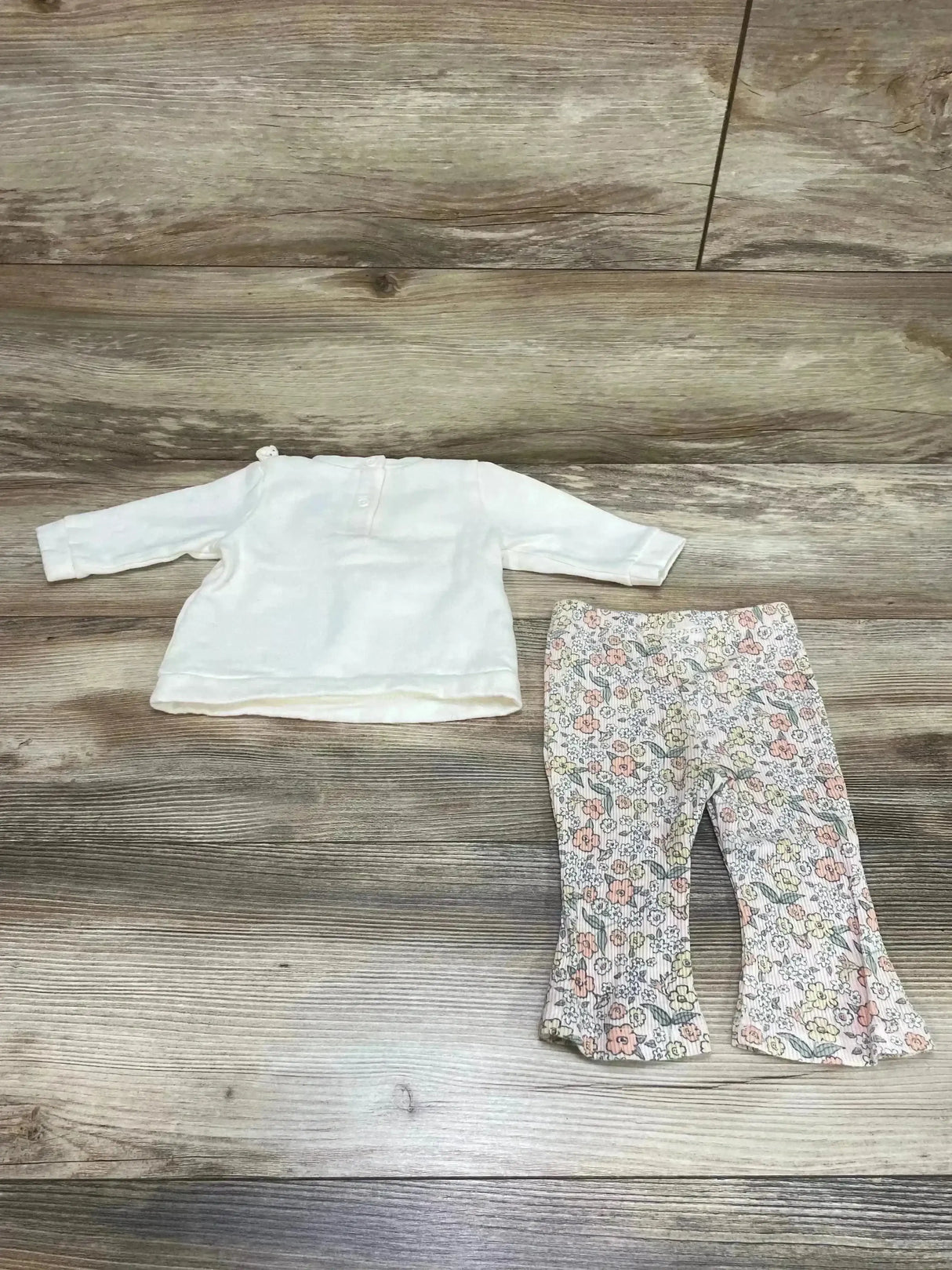 Flat lay of Nicole Miller cream long-sleeve sweatshirt and floral ribbed flared leggings, size 3–6 months on wood floor