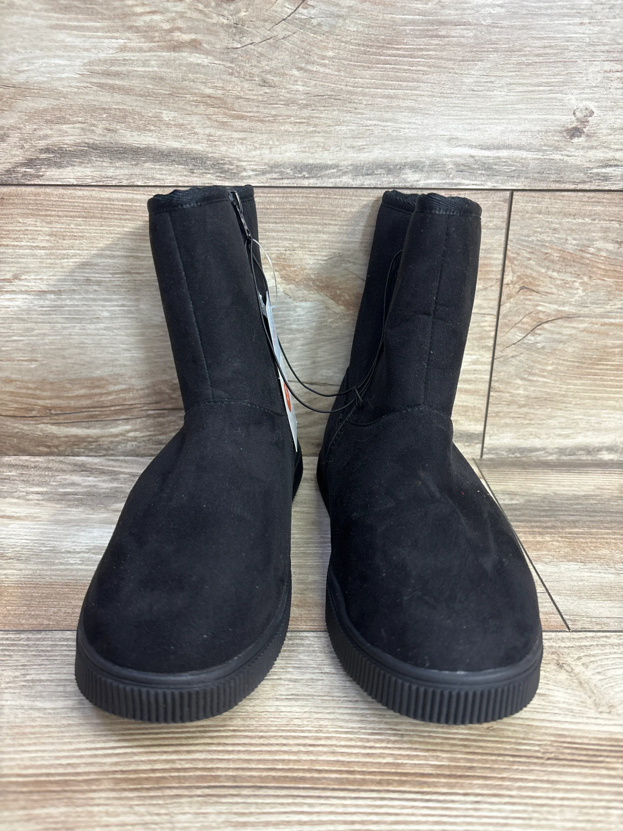 Pair of black suede kids boots with rubber soles on wood floor