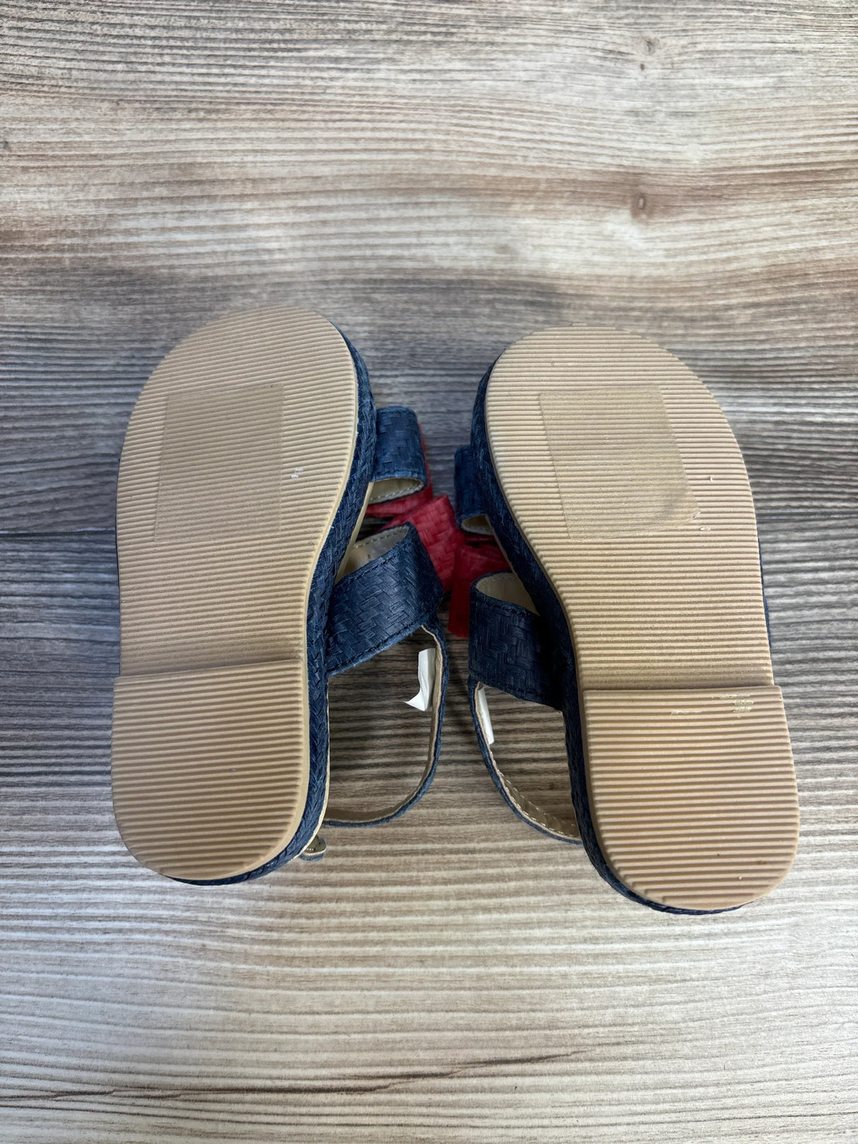 Sole view of Janie and Jack Double Bow Straw Sandals in navy with tan rubber soles on wood plank floor