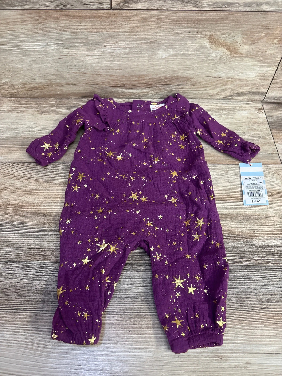 Purple baby romper with gold star pattern, long sleeves, laid on wood background