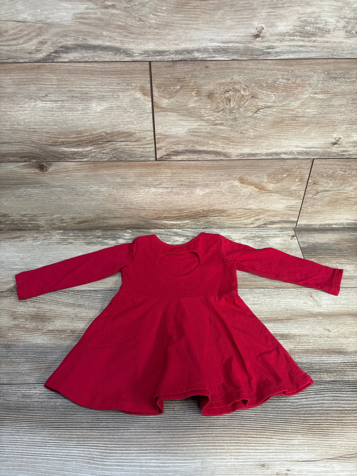 Front view of red long sleeve dress with flared skirt and heart-shaped neckline cutout, laid on wood-look flooring