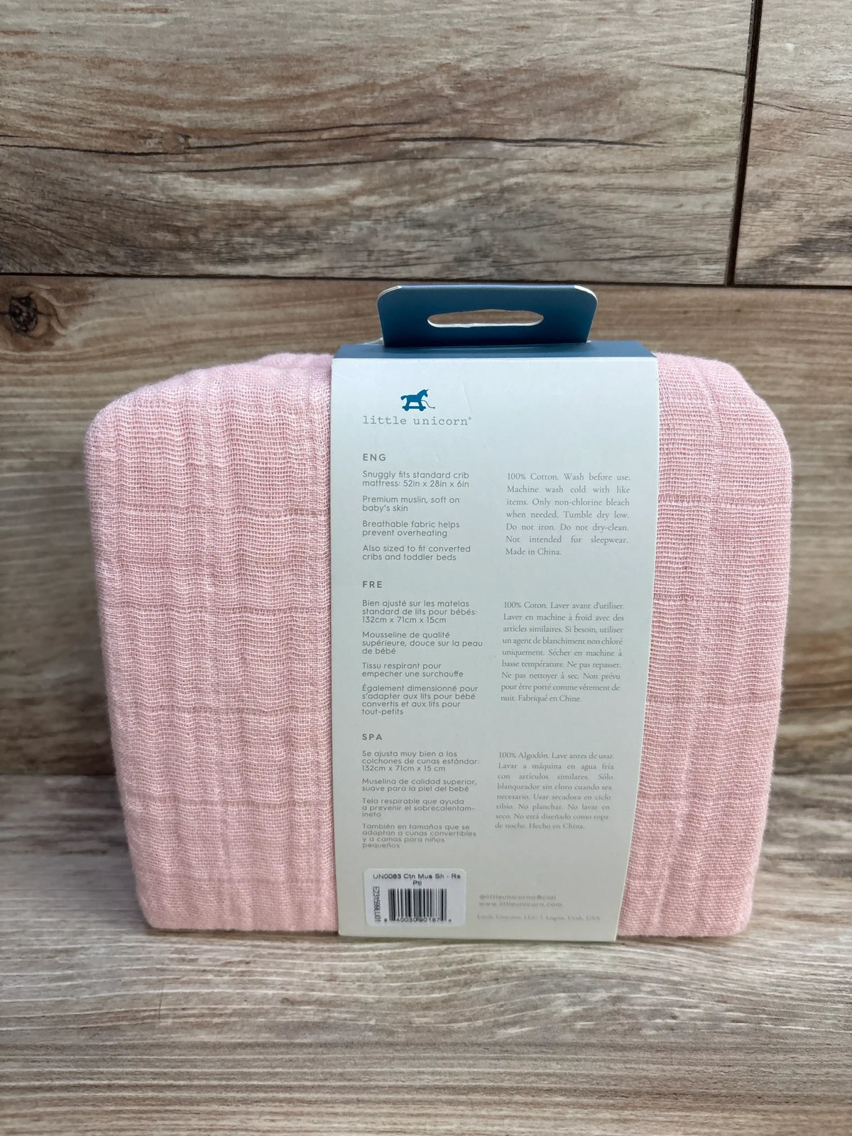 Front view of folded pink Little Unicorn muslin crib sheet in packaging on wood background