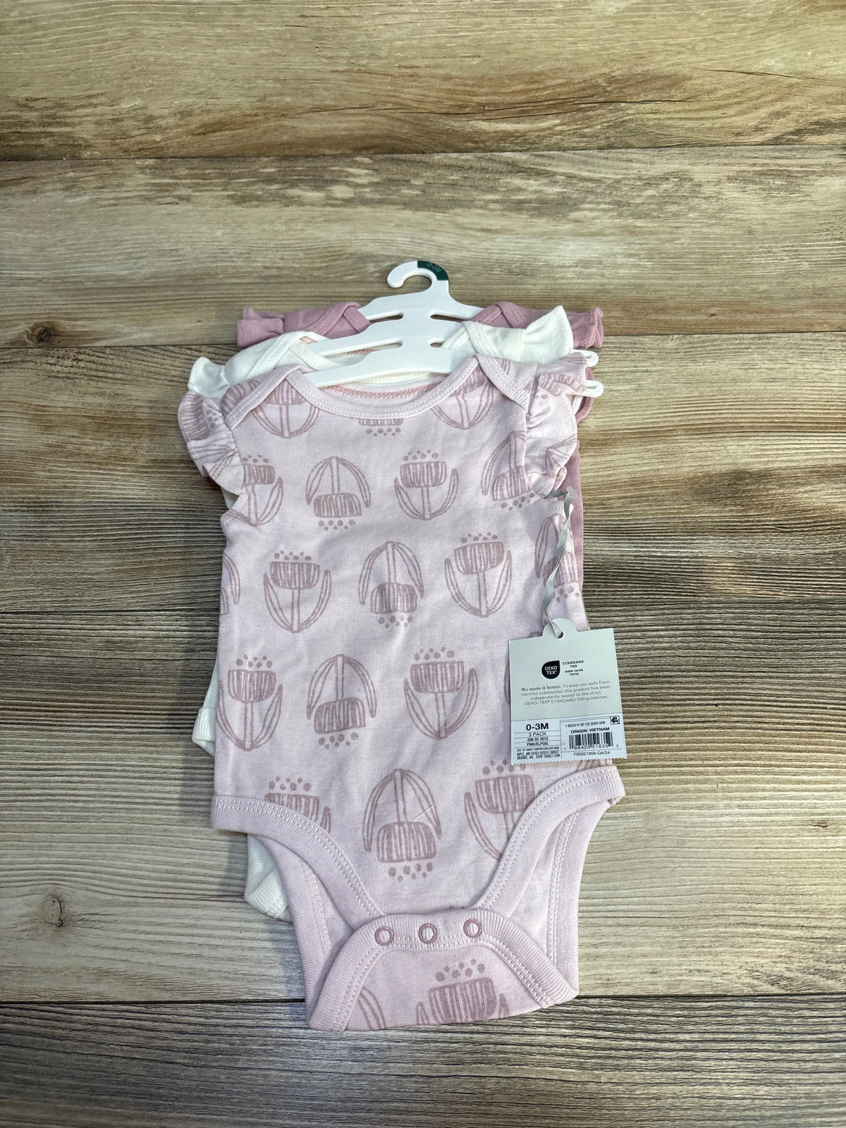 Front view of three pink Cloud Island sleeveless bodysuits with flower pattern and snap closures, displayed on hangers over wood