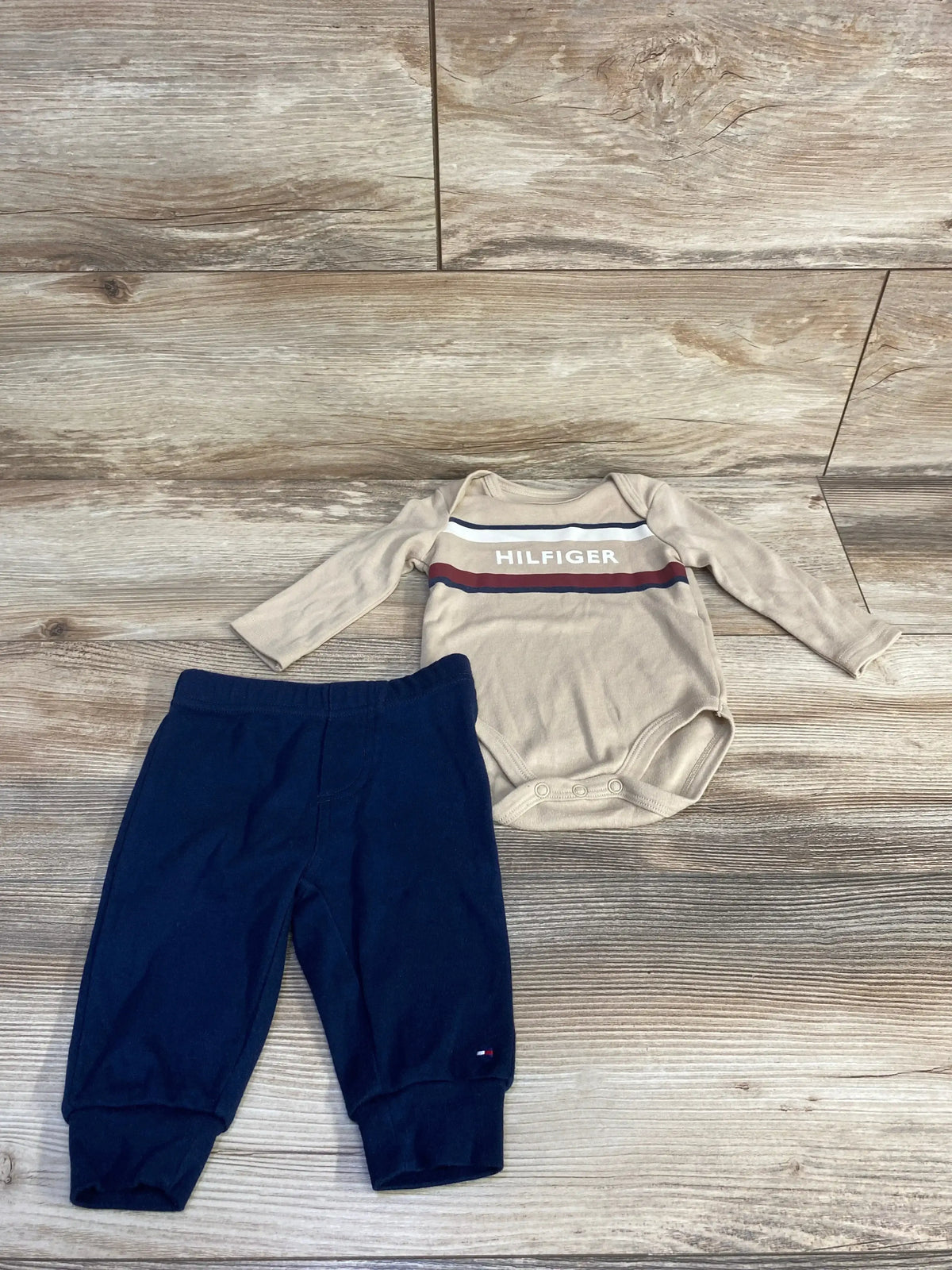 Front view of newborn beige Tommy Hilfiger two-piece set showing striped long-sleeve bodysuit and matching pants on white background