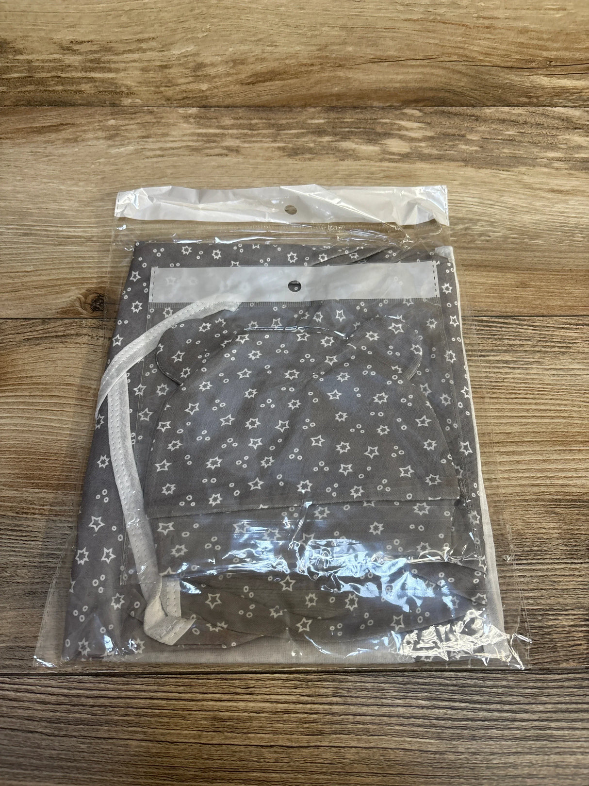 Top-down view of grey star-print newborn swaddle wrap with matching bear-ear hat packaged in clear plastic on wooden surface