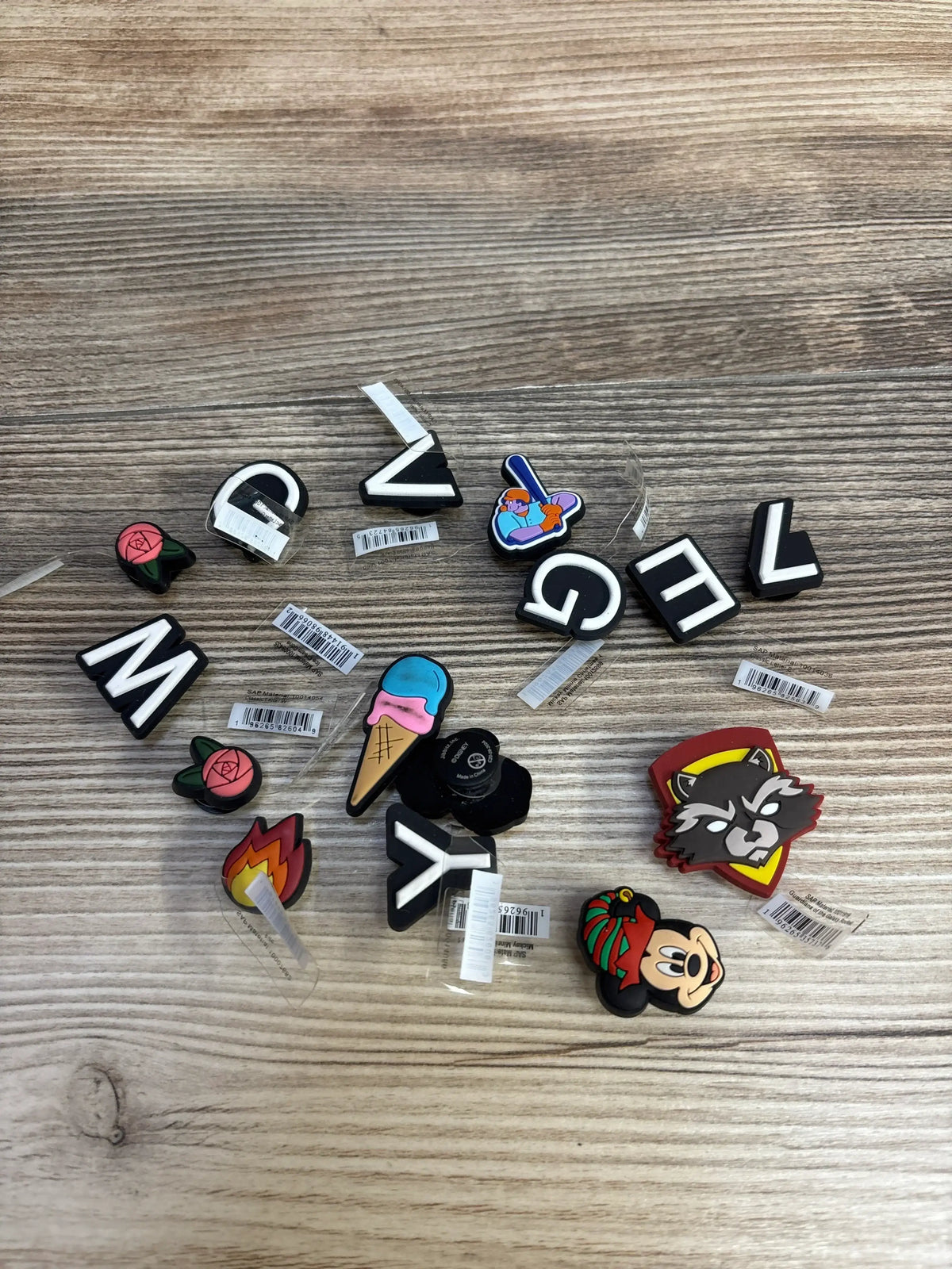 Crocs Jibbitz shoe charms with letters, ice cream, rose, raccoon, and cartoon character on wooden surface