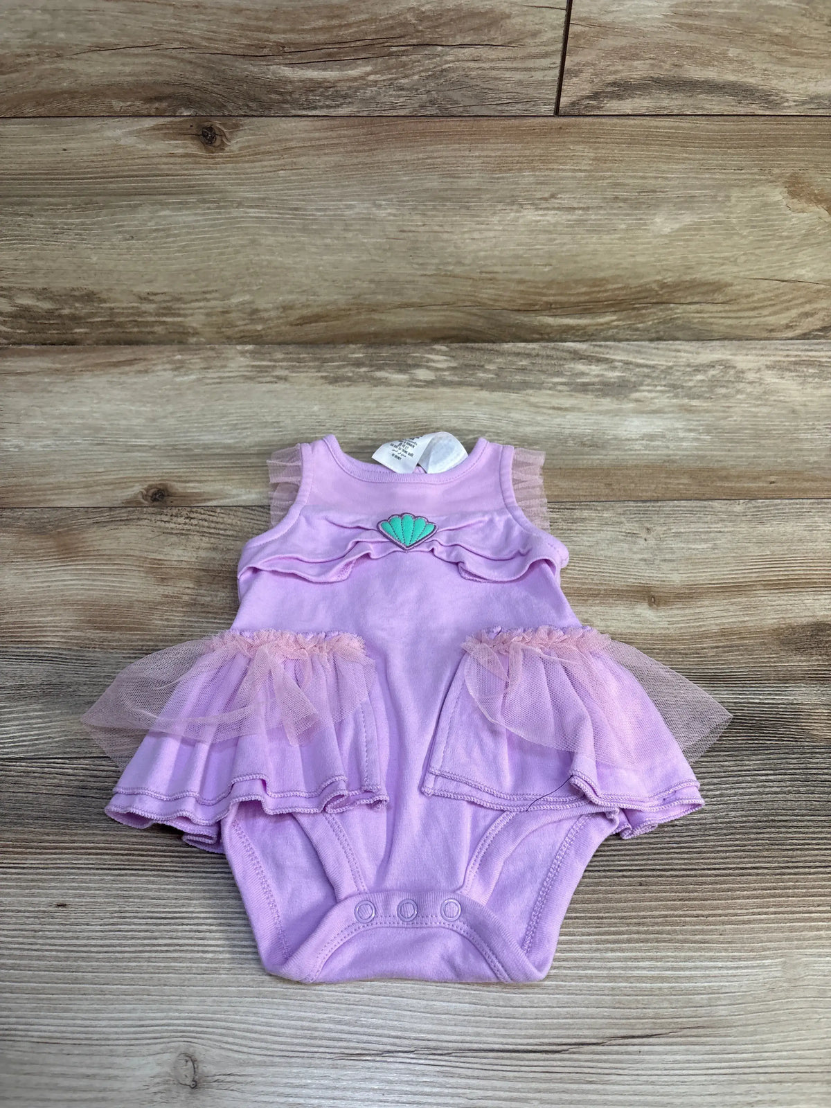 Front view of Disney Store purple Little Mermaid tutu bodysuit with ruffled mesh skirt and seashell detail on wood background